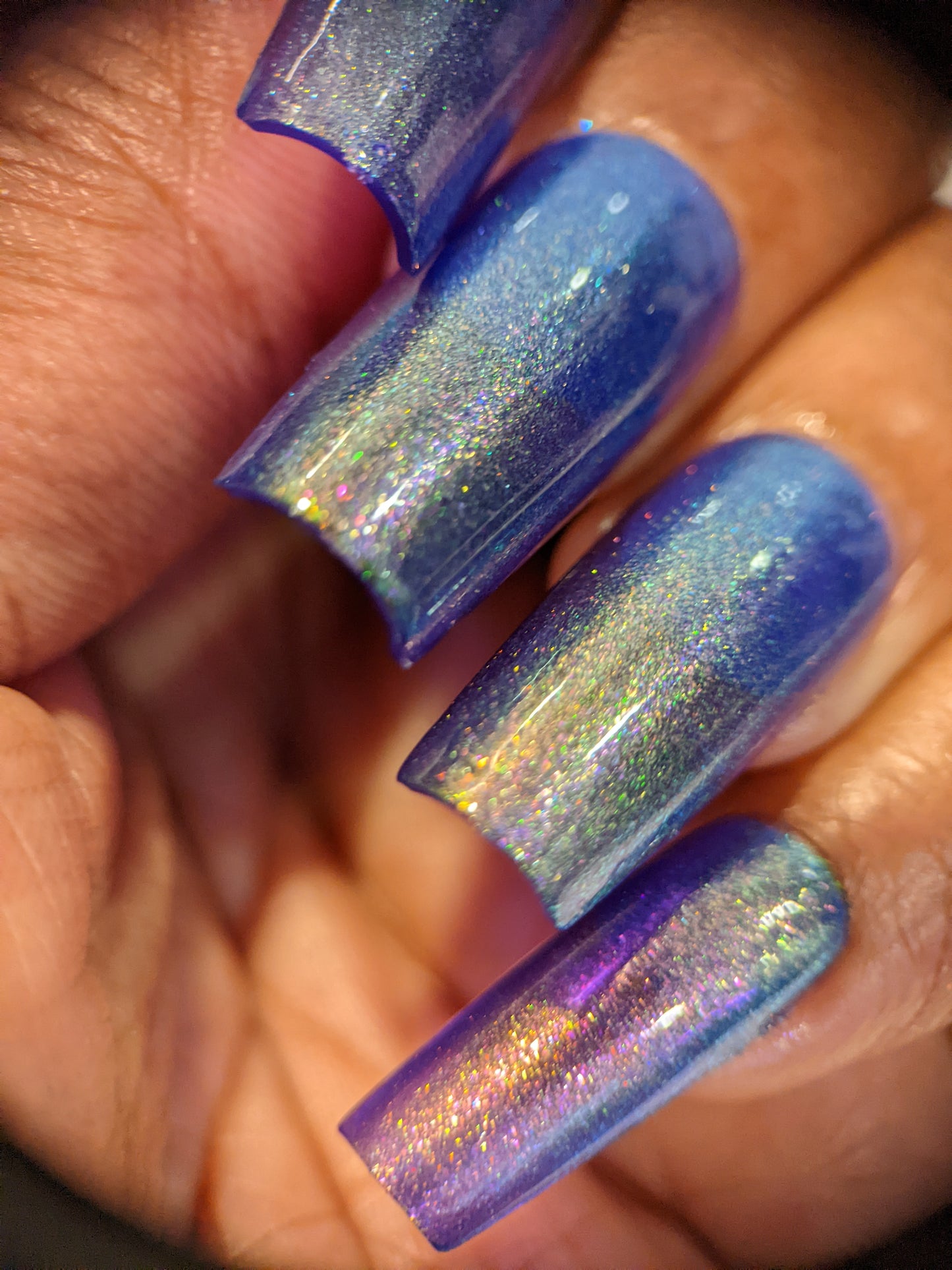 A close-up of a hand adorned with PI Colors' "90s Kind of World Purple Nail Polish" highlights the aurora pigments that shimmer with a gradient finish. The long, rectangular nails catch the light to exhibit a sparkling effect, perfectly capturing the iridescent charm of this handmade polish.
