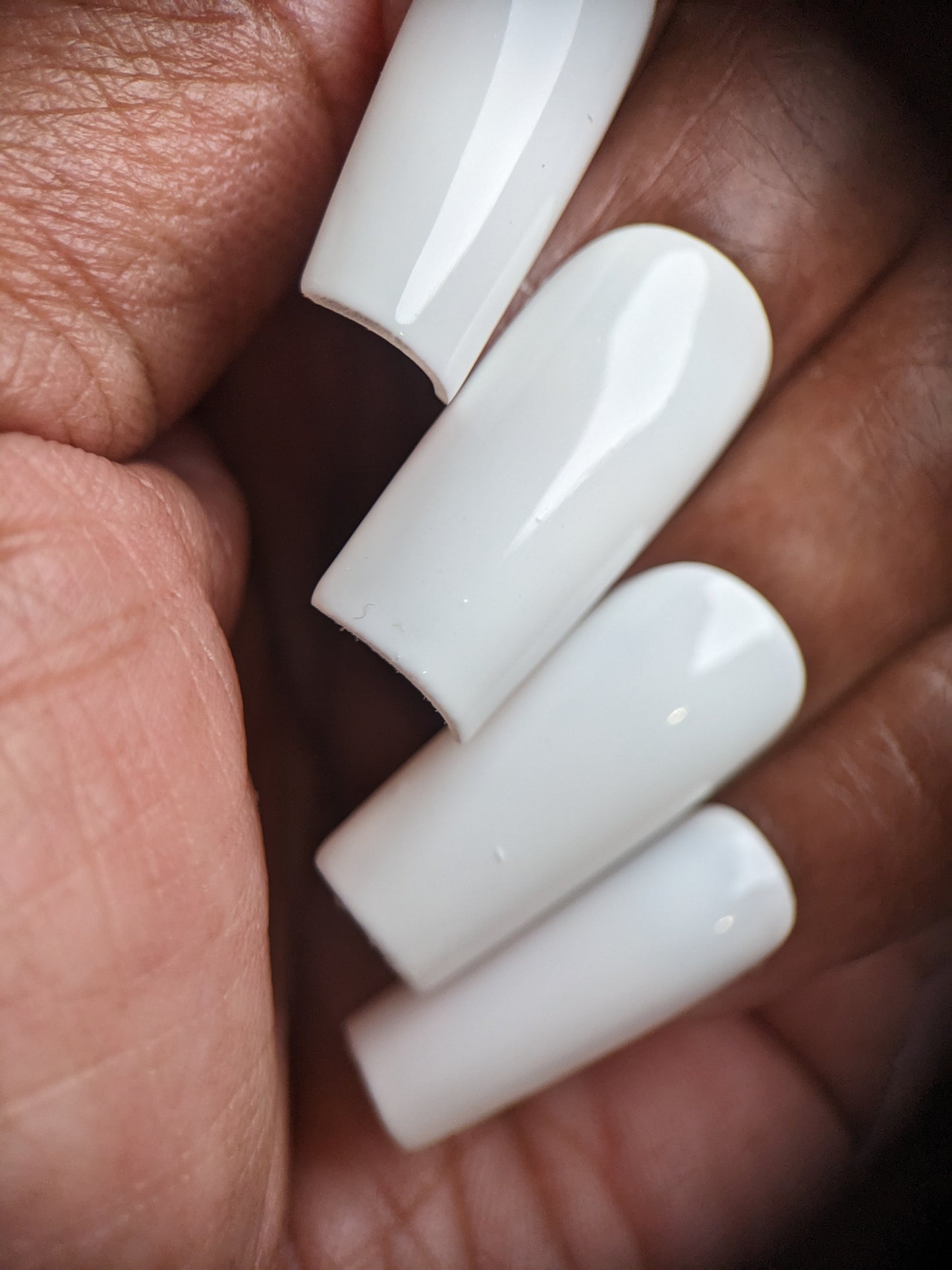 Close-up of a person's hand highlighting white, coffin-shaped nails with a glossy creme finish using Bright White.223 White Nail Polish by PI Colors. The long, well-manicured nails featuring 10-free polish rest against a palm with a natural skin tone.