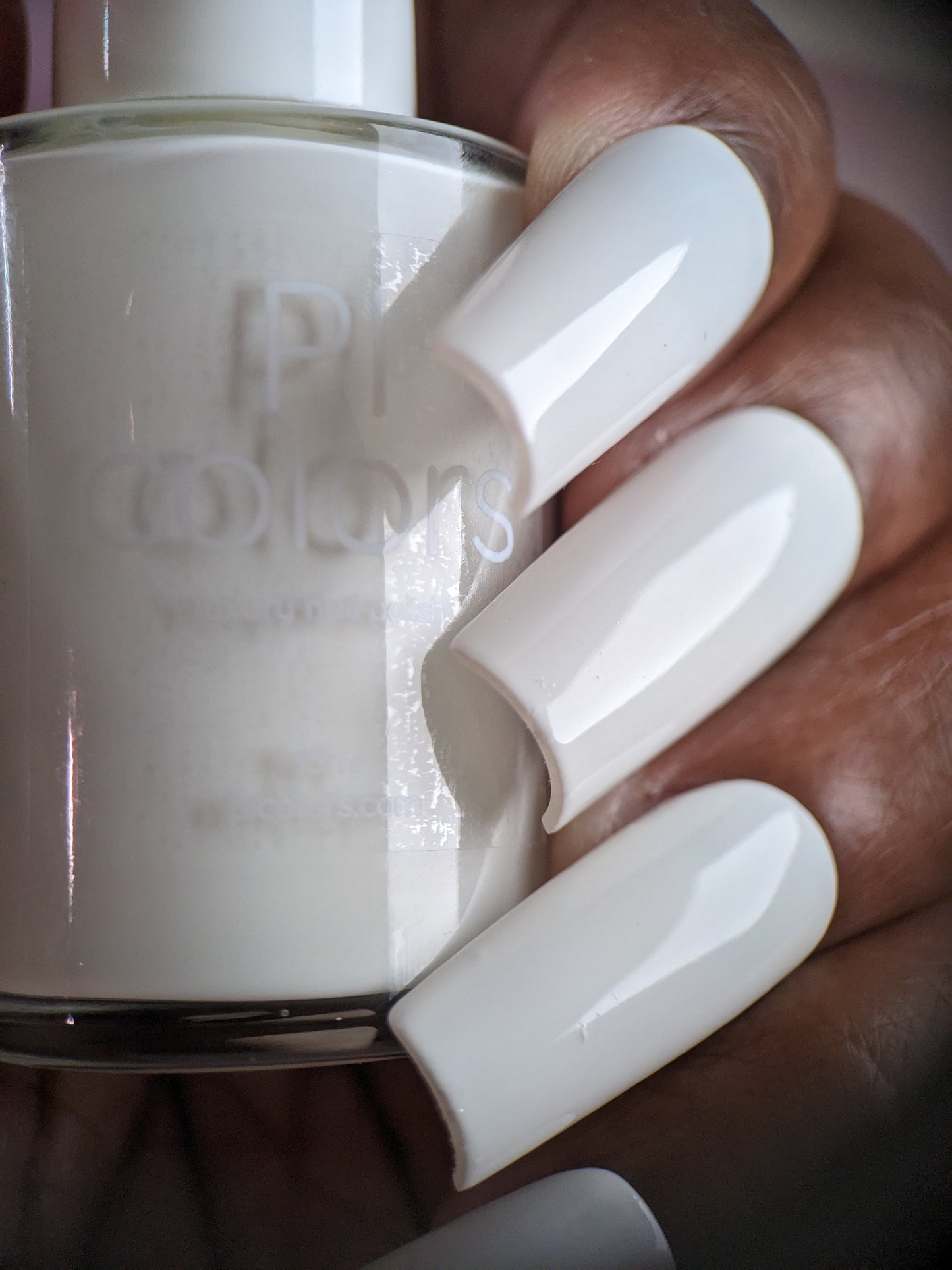 Close-up of a hand holding a bottle of PI Colors' Bright White.223 White Nail Polish. The nails, painted in the same glossy creme finish, match the polish in the bottle perfectly and are long and shiny.