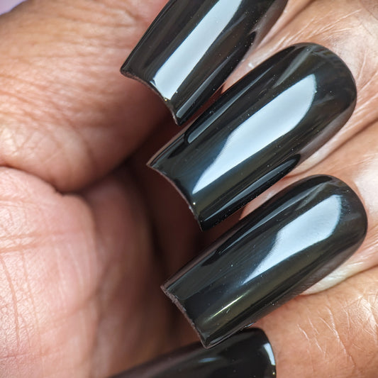 Close-up of a hand with long nails painted using PI Colors' Onyx.274 Black Nail Polish, which features a glossy, 10-free formula. The well-shaped nails have a smooth, reflective surface that resembles a glossy crème finish. The warm skin tone of the hand enhances their striking allure, making the nails the focal point of the image.