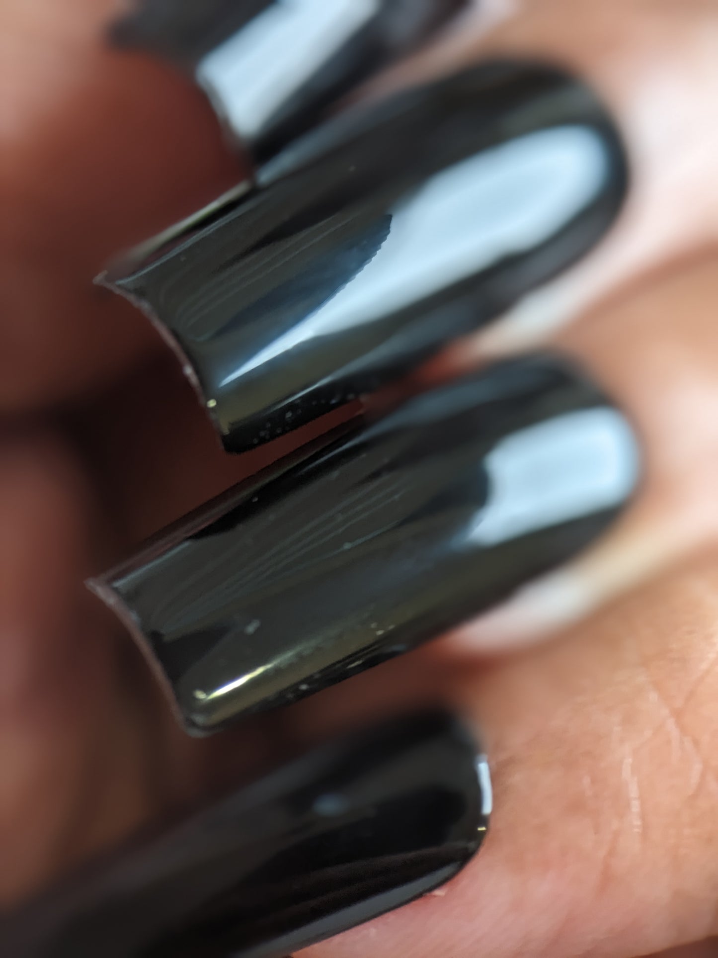 A close-up of hands with long nails features the PI Colors Onyx.274 Black Nail Polish, presenting a glossy creme finish that reflects light beautifully and results in a smooth manicure.