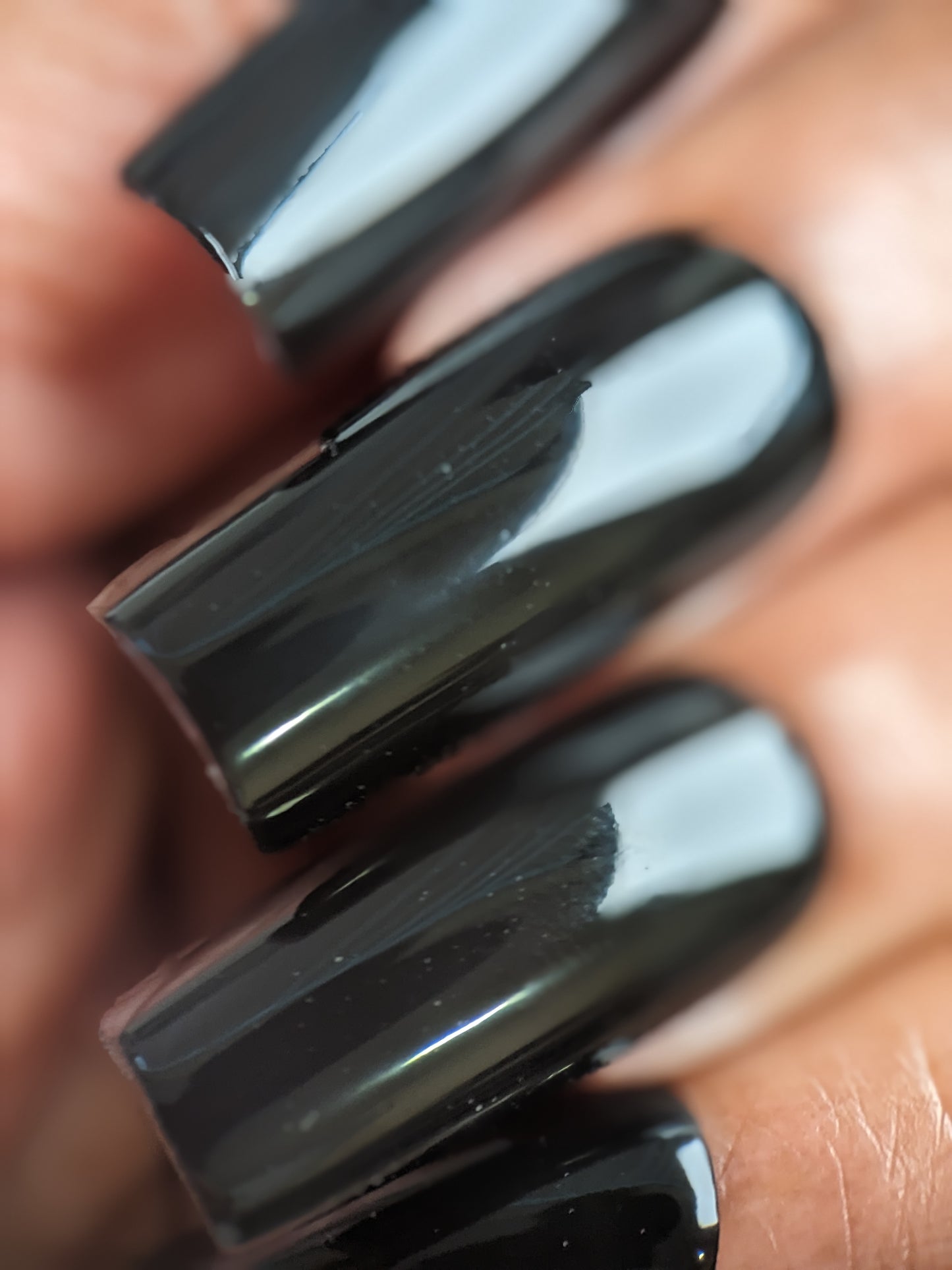 Close-up of neatly manicured fingernails adorned with Onyx.274 Black Nail Polish by PI Colors. The glossy crème finish beautifully reflects light, highlighting the smooth, polished surface.