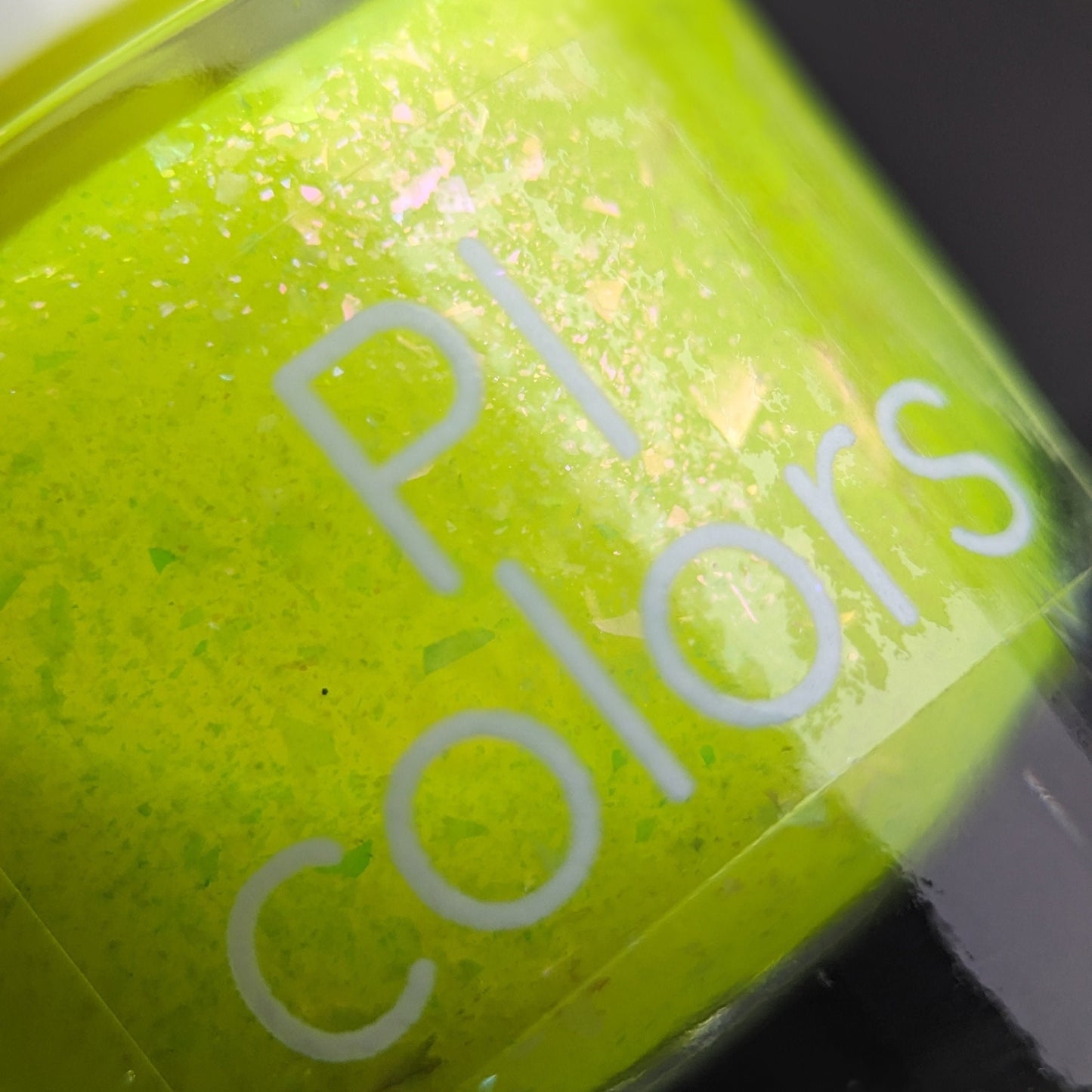 Close-up of a bottle labeled "Neon Shine Yellow" by PI Colors, highlighting luxury nail lacquers in neon yellow-green with subtle glitter particles.