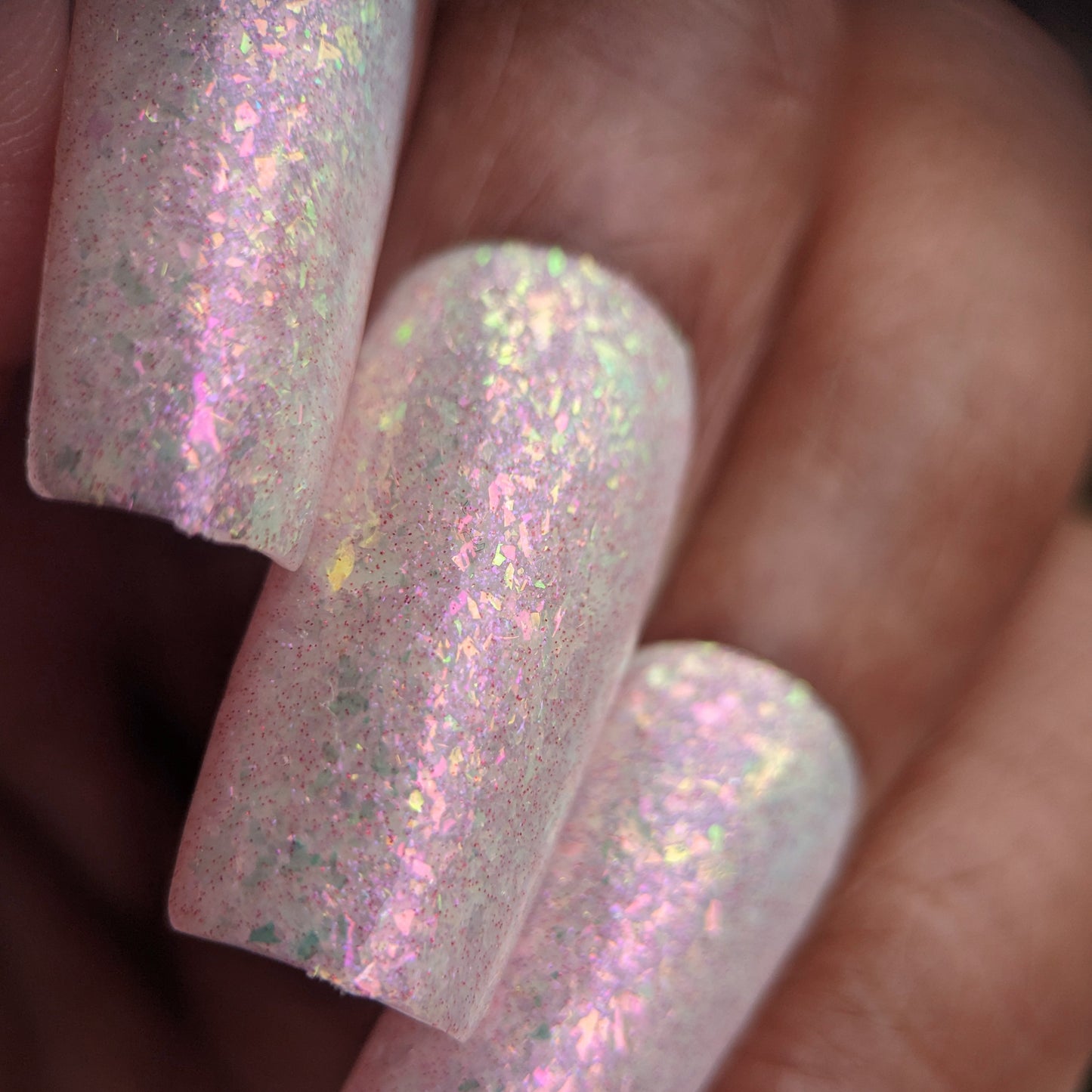 Close-up of manicured nails with Caelestis Dreams.005 by PI Colors—a pastel iridescent polish with a pinkish hue and shimmering rainbow flakies creating a subtle sparkle.