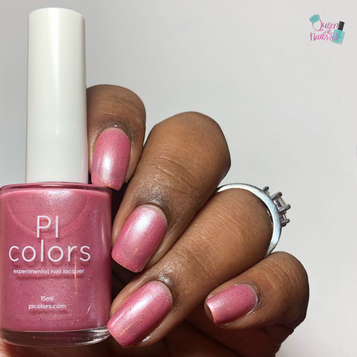 A hand adorned with a silver ring flaunts nails painted in Roseate Bliss.012 Pink Nail Polish, enhanced with holographic glitters from a bottle labeled "PI Colors.