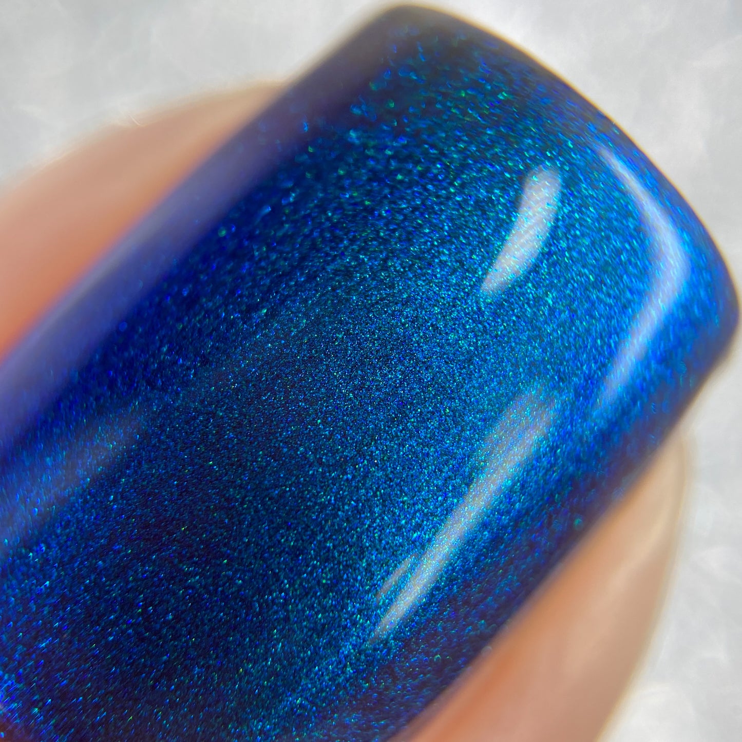 A close-up shot of a fingernail adorned with PI Colors' Aurora Blue.316 luxury nail lacquer showcases the shimmering polish reflecting light to create a lustrous, metallic effect.