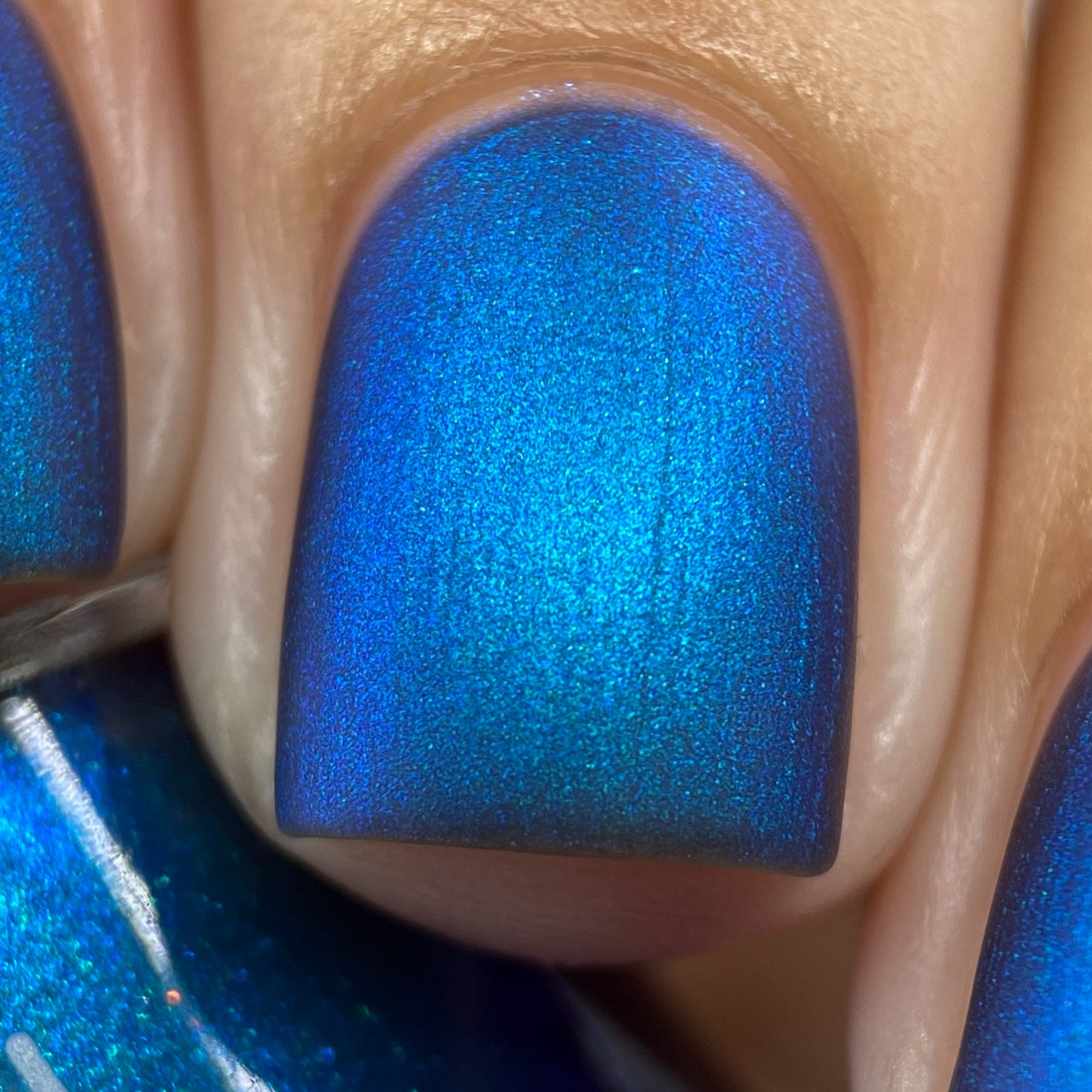 Close-up of a fingernail painted with PI Colors' Aurora Blue.316, a luxurious shimmering nail lacquer. The surface exhibits a matte, silky finish under bright lighting.