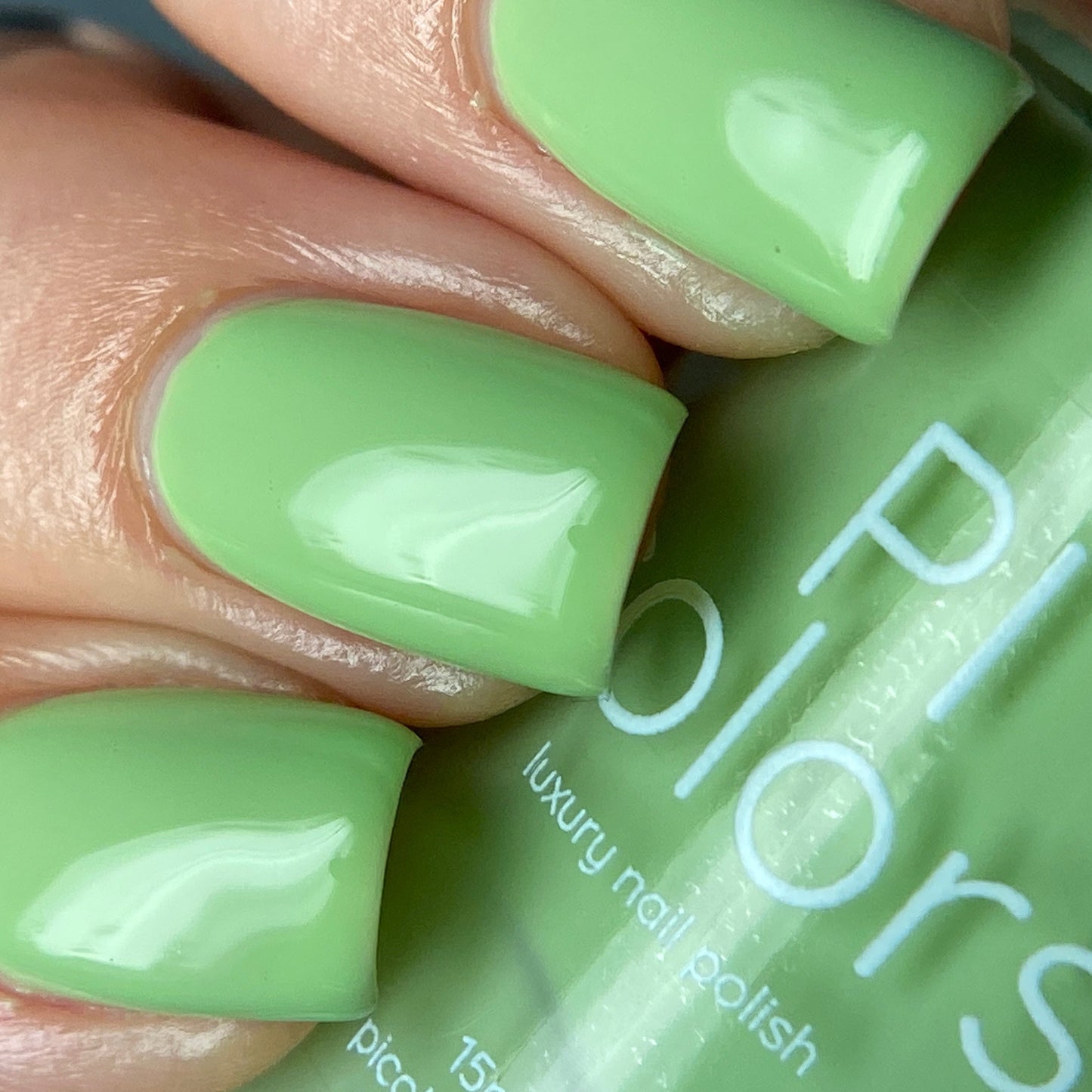 A close-up shot features a neatly manicured hand adorned with PI Colors' Pistachio.400 Green Nail Polish, gripping a partially visible bottle of the same luxury, handmade polish, which boasts a smooth, glossy finish.