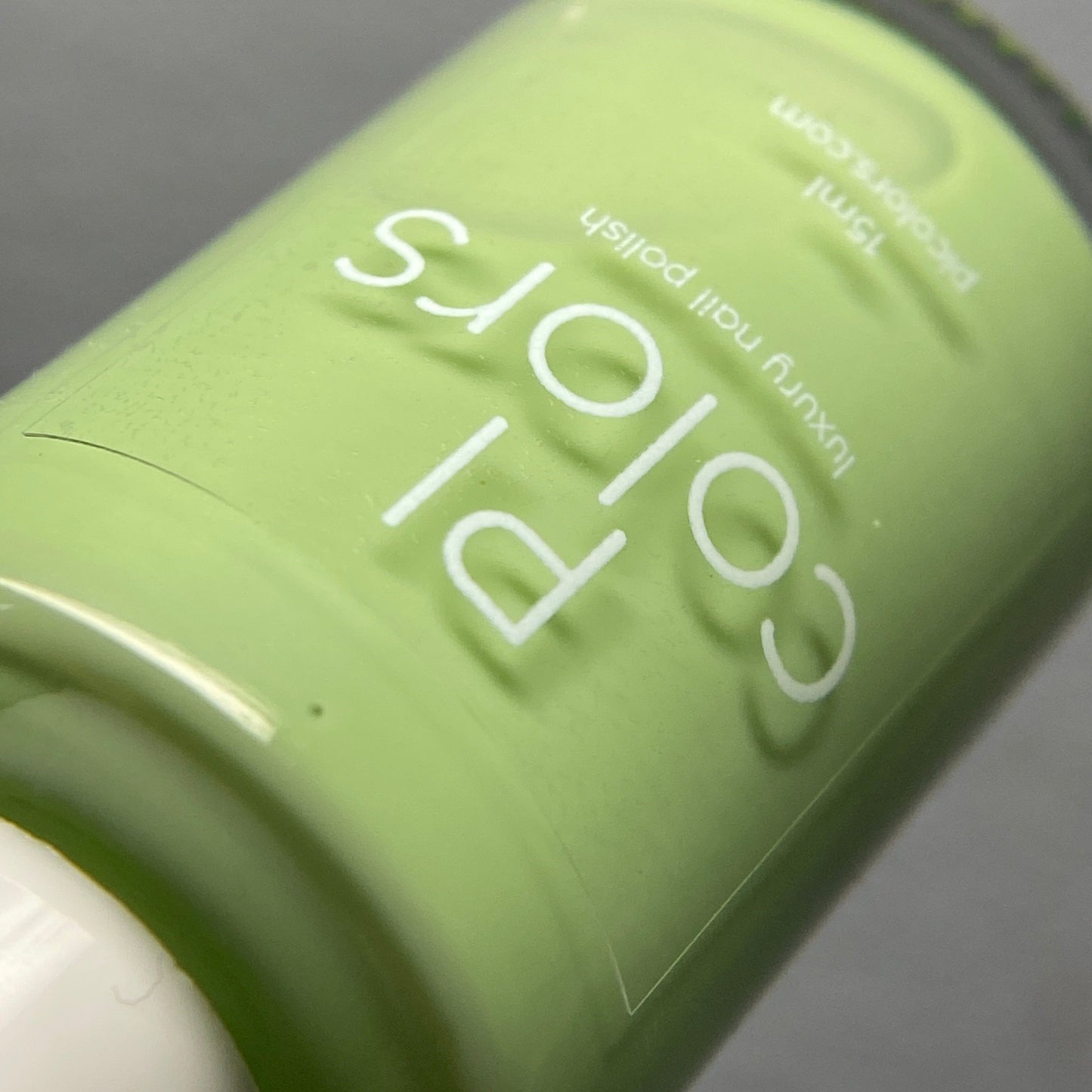 Close-up view of a light green bottle of Pistachio.400 Green Nail Polish by PI Colors, displaying "luxury nail polish" and "15ml" on the label. This creme finish bottle is elegantly tilted against a gray background.