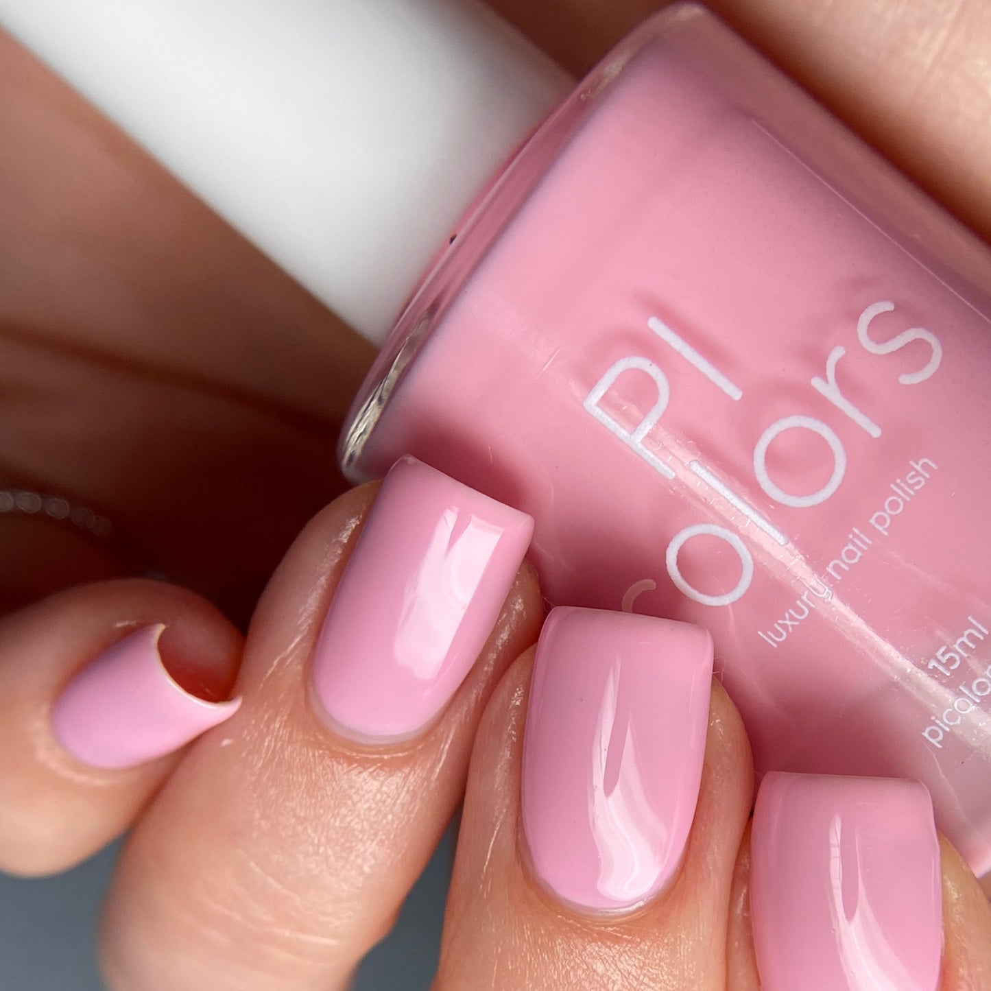 A close-up of a hand with manicured nails painted in the luxurious Cupcake.400 Pink Nail Polish by PI Colors, showcasing a glossy pastel pink finish. The well-shaped nails display a shiny, creme texture that beautifully complements the chic polish bottle.