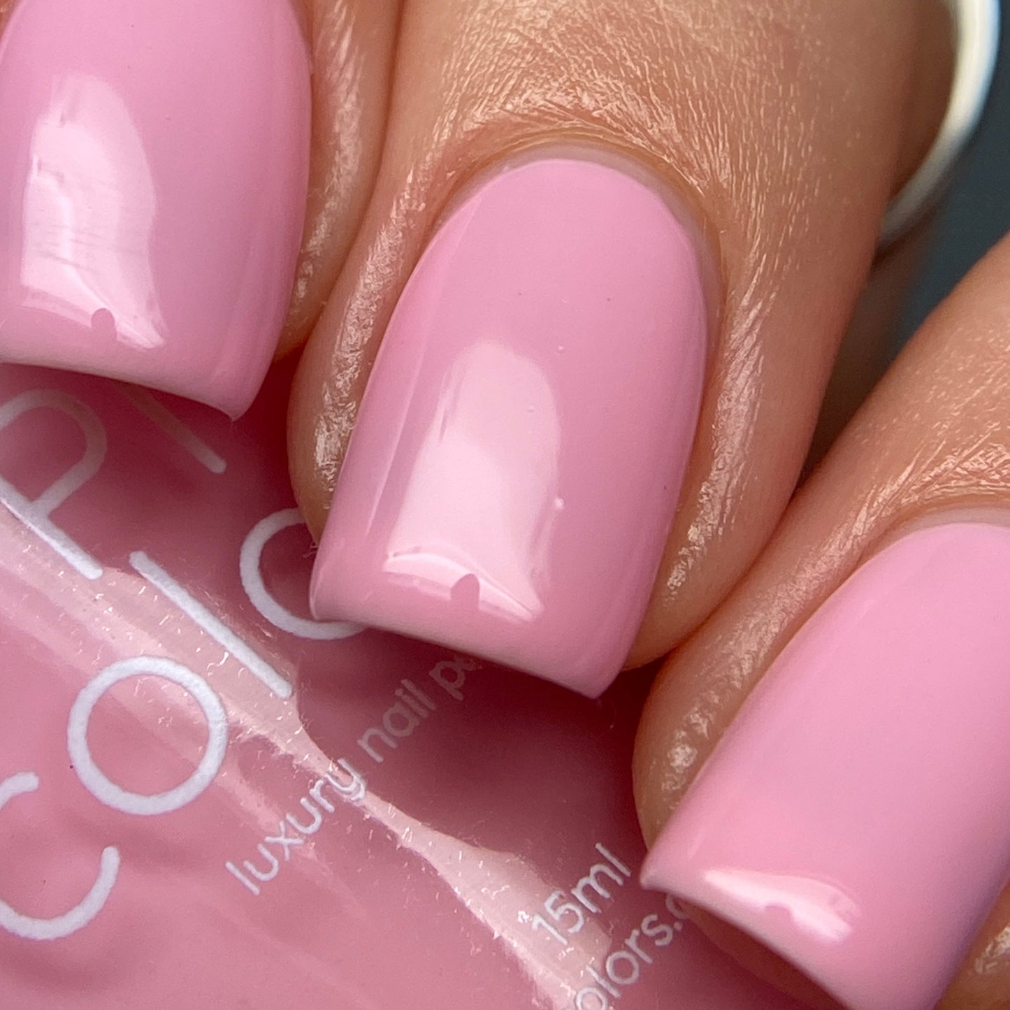 A close-up captures a hand with nails elegantly coated in the glossy **Cupcake.400 Pink Nail Polish** by **PI Colors**, showcasing their neat manicure as the smooth surface reflects light. The 10-free bottle label is slightly visible, revealing the word "color" and indicating a volume of "15ml".
