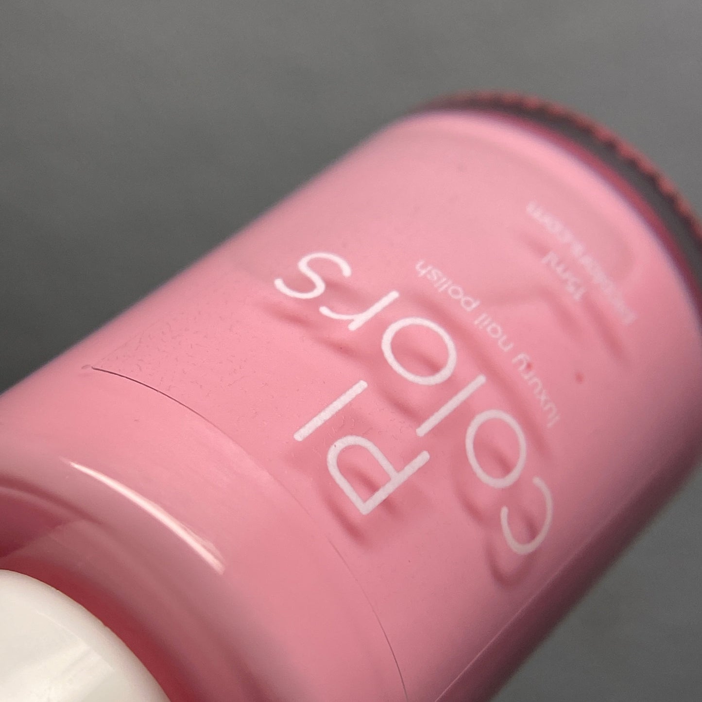 A close-up of a bottle of "Cupcake.400 Pink Nail Polish" by PI Colors, featuring pastel pink color and tilted to emphasize the brand name along with the description "luxury nail lacquer" on its surface. The white cap contrasts beautifully with the soft pink hue, highlighting its luxurious creme finish.