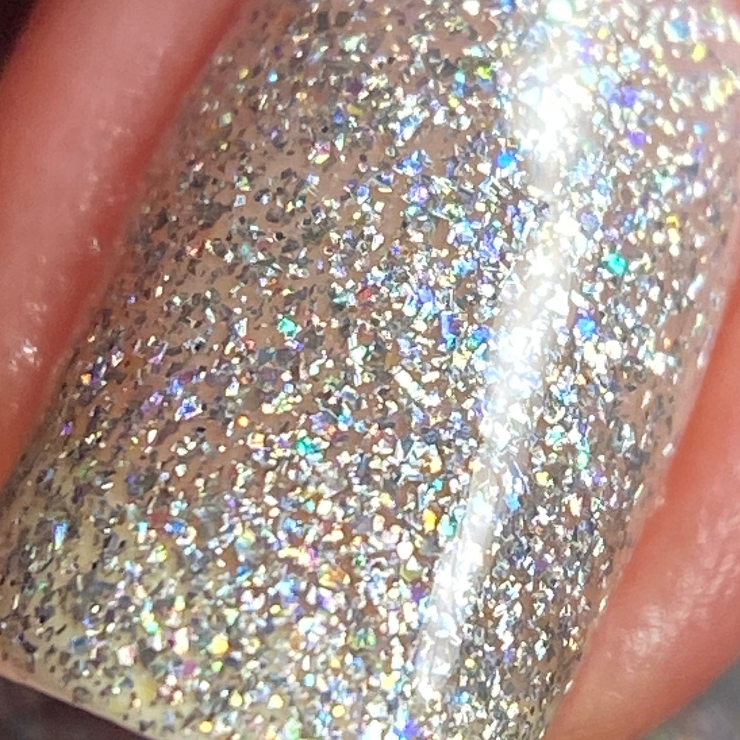 The image showcases a fingernail decorated with the Diamond Blast.401 Silver Holographic Glitter Nail Polish Topper by PI Colors. This 10-free luxury product shimmers brilliantly, displaying blue and pink hues under light thanks to its dazzling iridescent texture.