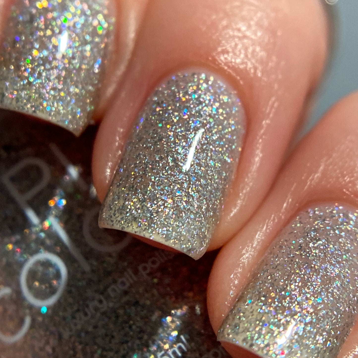 Close-up of fingernails adorned with PI Colors' Diamond Blast.401 Silver Holographic Glitter Nail Polish Topper. This luxurious topper reflects a rainbow of colors under the light, providing a glossy finish. These meticulously manicured nails highlight the allure of flawless, handmade nail polish artistry.