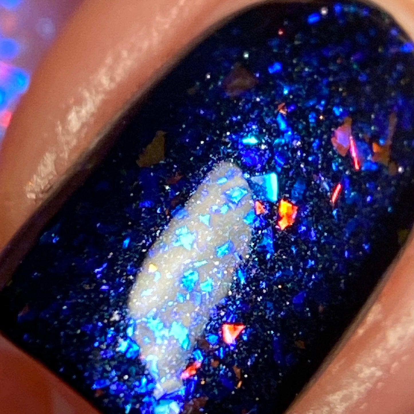 Close-up of a fingernail adorned with PI Colors' Pink Sapphire.404 Pink Nail Polish Topper, featuring colorshifting flakie and dark blue glitter polish. The iridescent nail polish creates a reflective sheen, revealing an enchanting mix of blue, red, and white sparkles.