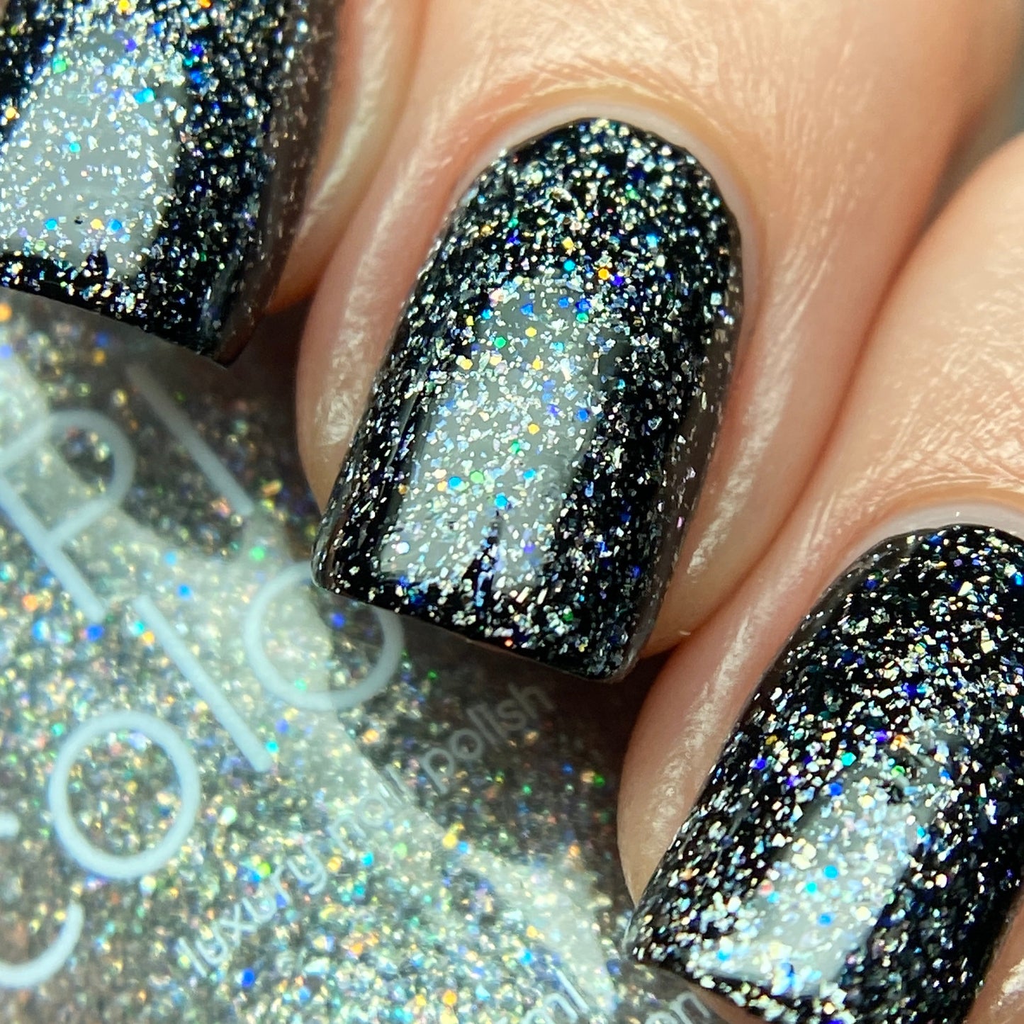 Close-up of fingernails adorned with a glossy black luxury nail lacquer, enhanced by the captivating shimmer of holographic glitter. In the background, a bottle labeled "Diamond Blast.401 Silver Holographic Glitter Nail Polish Topper" from PI Colors can be seen, perfectly matching the nails’ dazzling finish.