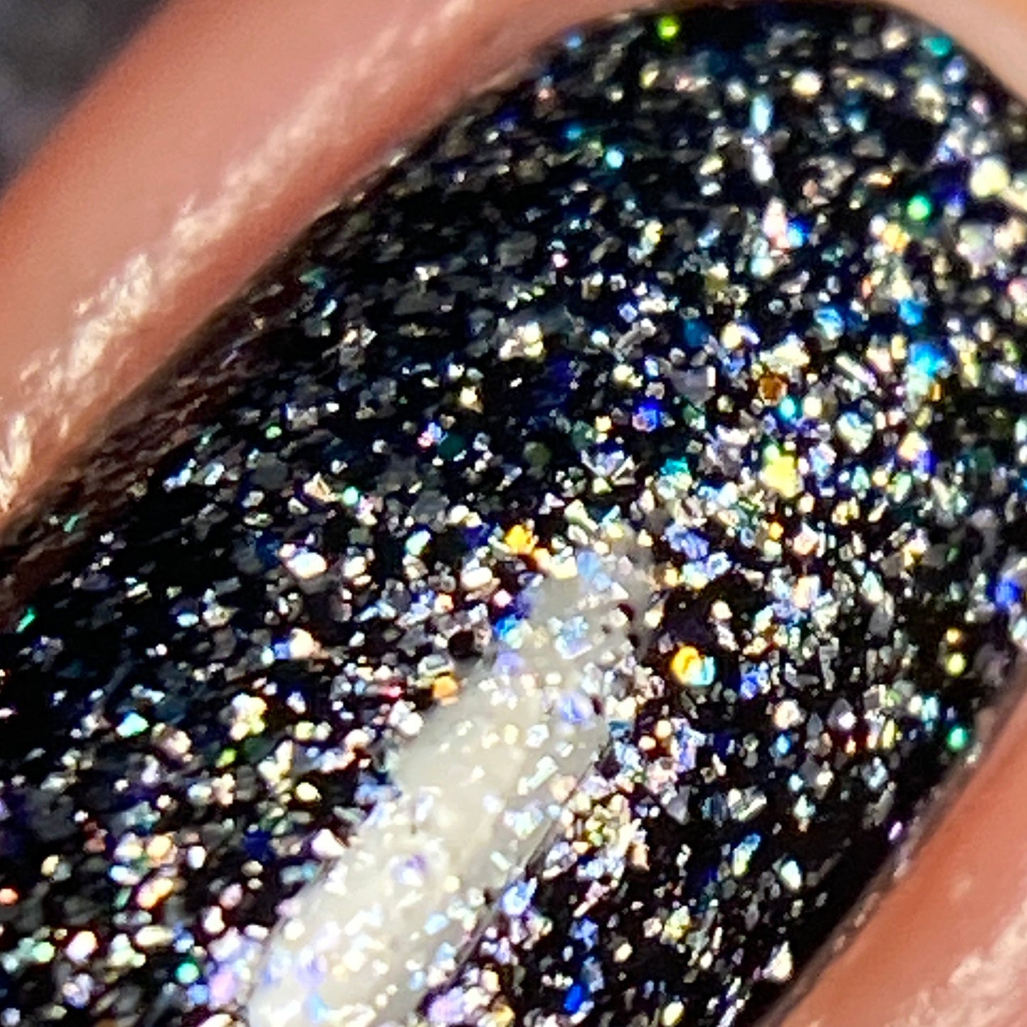 A close-up of a fingernail features luxury black nail lacquer enhanced with PI Colors' Diamond Blast.401 Silver Holographic Glitter Nail Polish Topper. The glitter creates a prismatic effect, reflecting various bright colors with a dazzling sparkle.