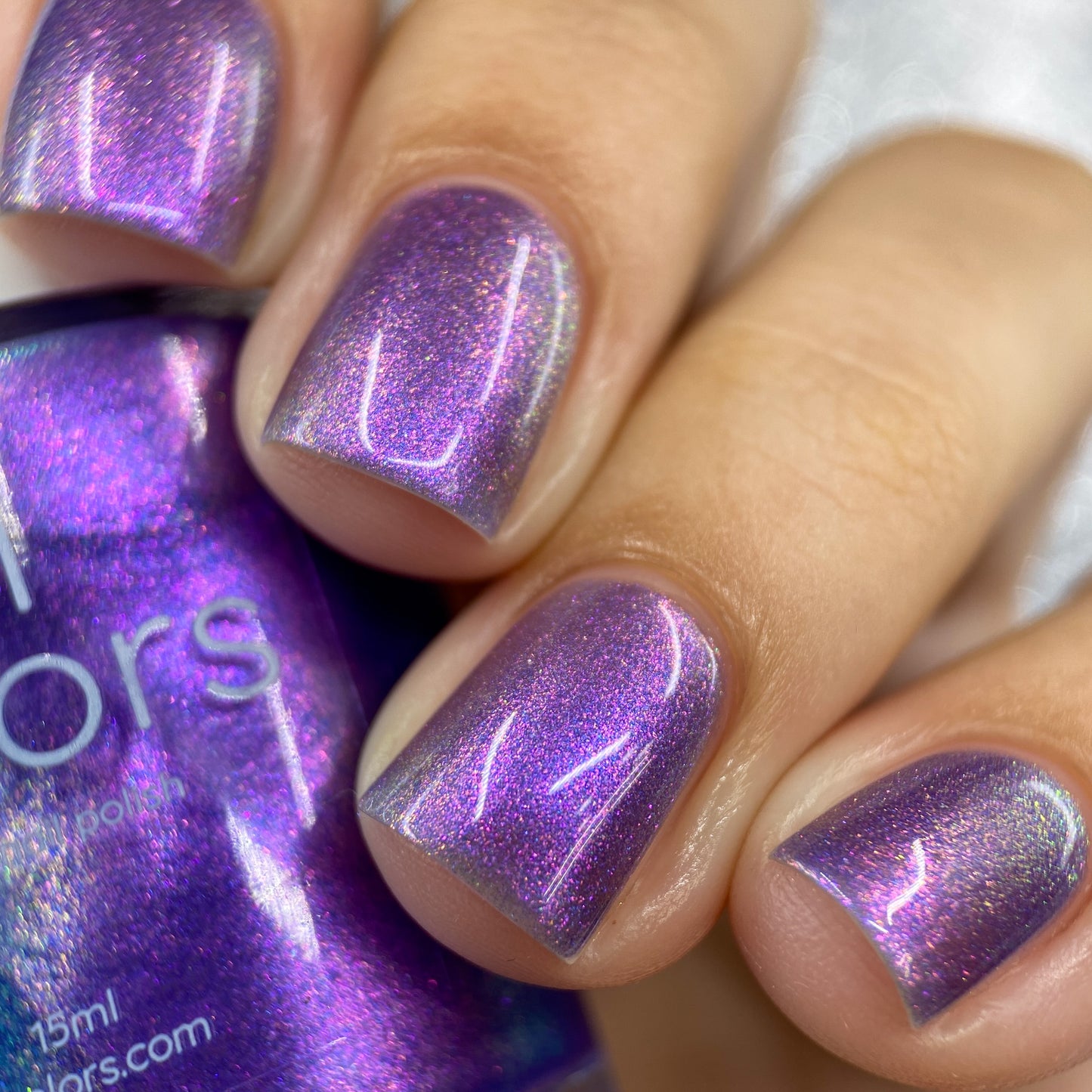 Fingers decorated with a glossy coating of Dusk Rainbow.321 Purple Nail Polish exhibit a neat manicure, their deep purple hue catching the light beautifully. Positioned in the background is a partially visible PI Colors bottle, its 10-free formula flawlessly matching this enchanting shade.