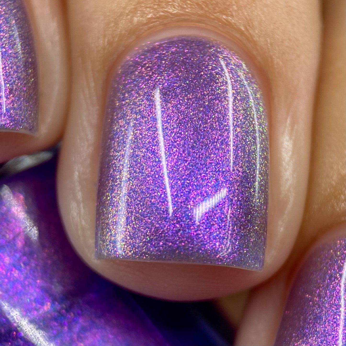 A close-up of a fingernail adorned with PI Colors' Dusk Rainbow.321 Purple Nail Polish showcases a shimmering aurora effect that sparkles with shades of purple and pink under the light. The nail is neatly manicured, ensuring peace of mind with its 10-free formula.