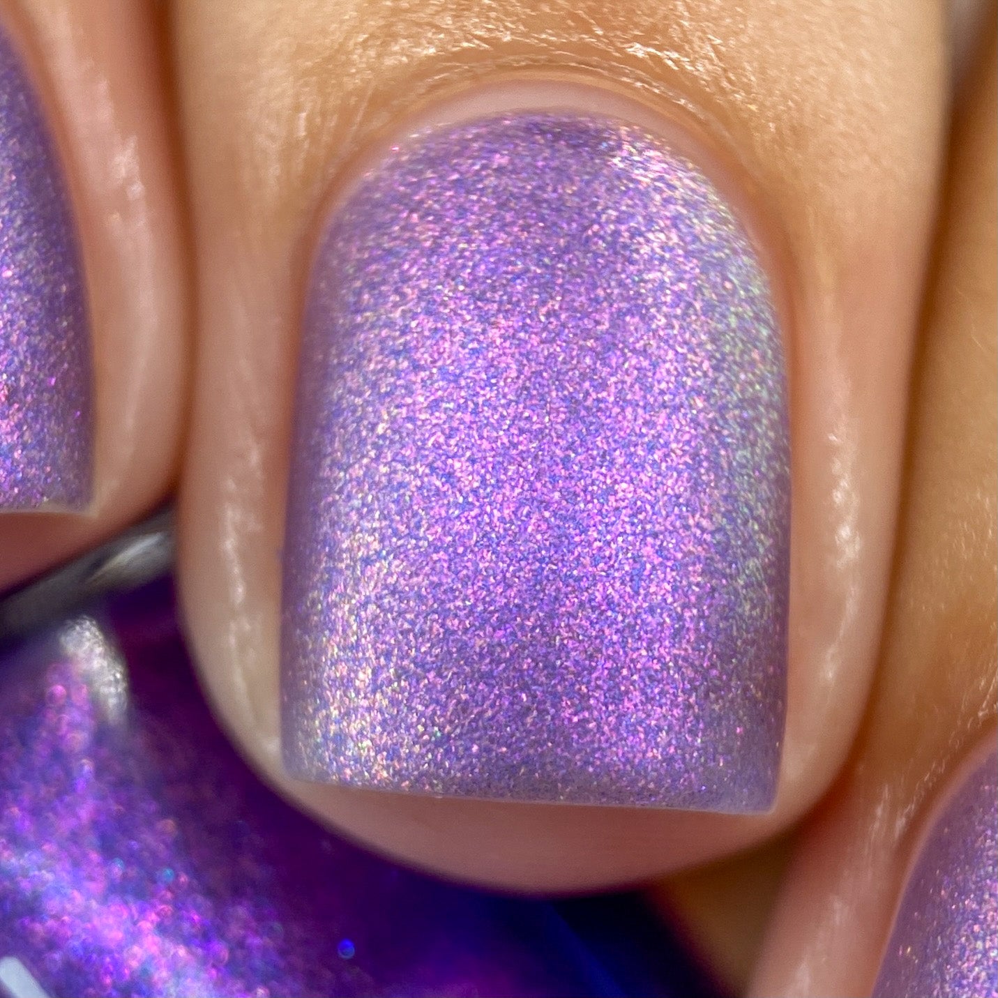A close-up of fingernails showcases the Dusk Rainbow.321 Purple Nail Polish by PI Colors, featuring a deep purple hue that transitions to pink and blue under the light. This handmade polish offers a smooth, glossy finish, accentuating the cyan and green shimmer within its vibrant and sparkly colors.