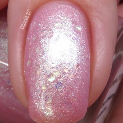 Close-up of a fingernail adorned with PI Colors' Pink Candy.210 Pink Nail Polish, which has glittery pink tones and iridescent flakes that reflect light to create a shimmering effect.