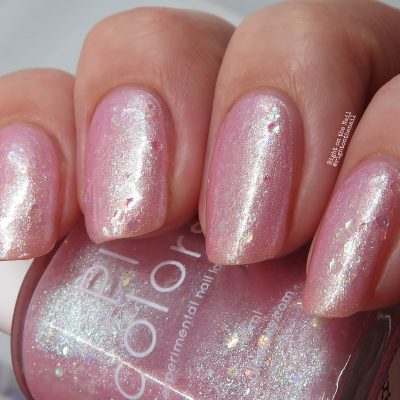 Close-up of a hand with nails painted in PI Colors' Pink Candy.210 Pink Nail Polish—a shimmering pastel pink jelly. The partially visible bottle showcases the same glossy finish, dotted with subtle sparkles that add an elegant touch.