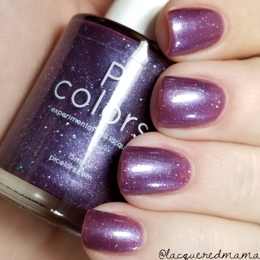 A hand with nails painted in the breathtaking shade named "Blackberry Dreams" holds a bottle of the same hue. The PI Colors bottle features this 10-free polish, enhanced with shimmery rainbow glitter that delivers captivating, sparkly accents.