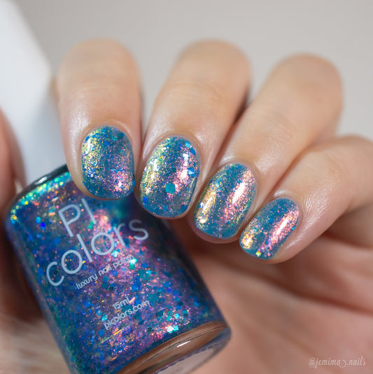 A hand with nails painted in a glittery blue polish featuring metallic blue holo glitter and iridescent pink, gold, and green flakes holds a bottle of Rainbow Quartz.000 by PI Colors, perfectly matching the stunning nail design.