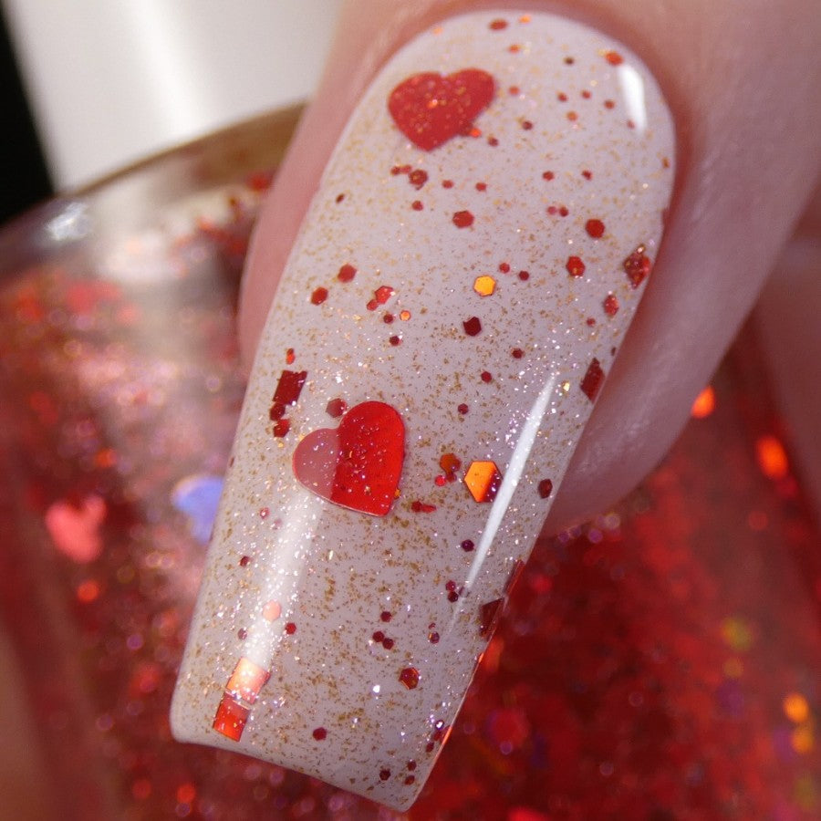 Close-up of a fingernail adorned with PI Colors' creamy, 10-free Strawberry Heart.208 nail polish topper, featuring red holographic hearts and hexagonal glitter. The background showcases a bottle of this red glitter nail polish, enhancing the vibrant, festive look.