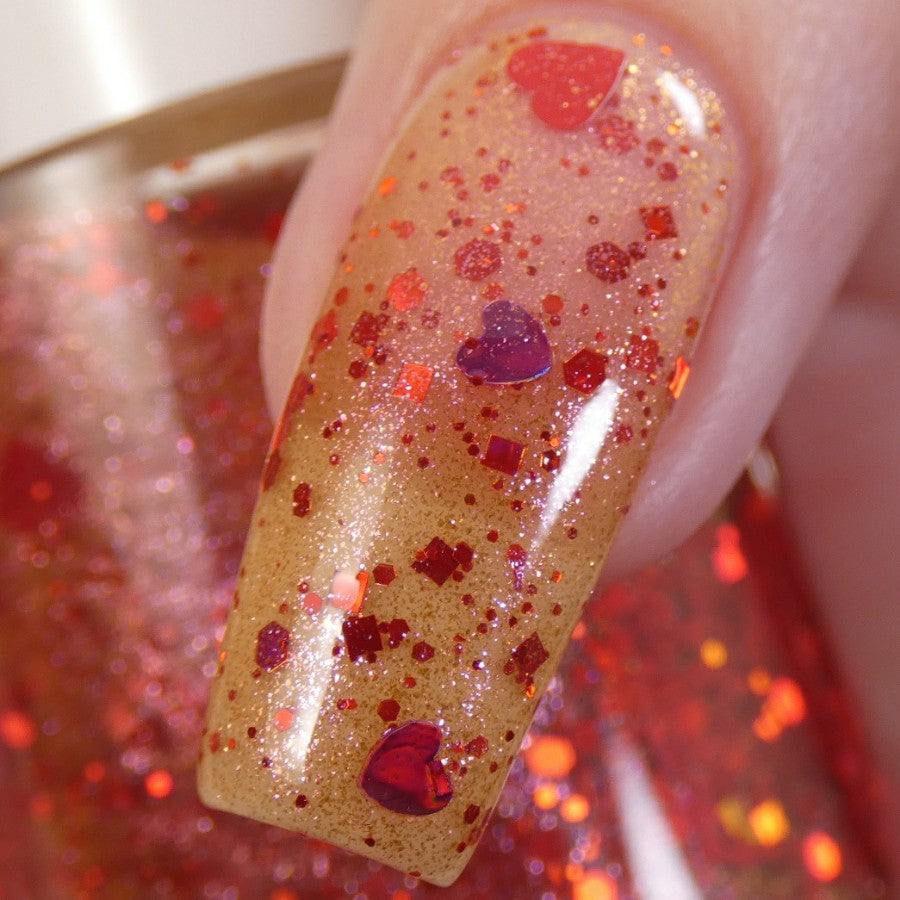 Close-up of a fingernail adorned with PI Colors' Strawberry Heart.208 Red Nail Polish Topper, showcasing its sparkling gold base, red glitter, and holographic heart-shaped accents. The polished surface catches the light, emphasizing the vibrant red and gold details.