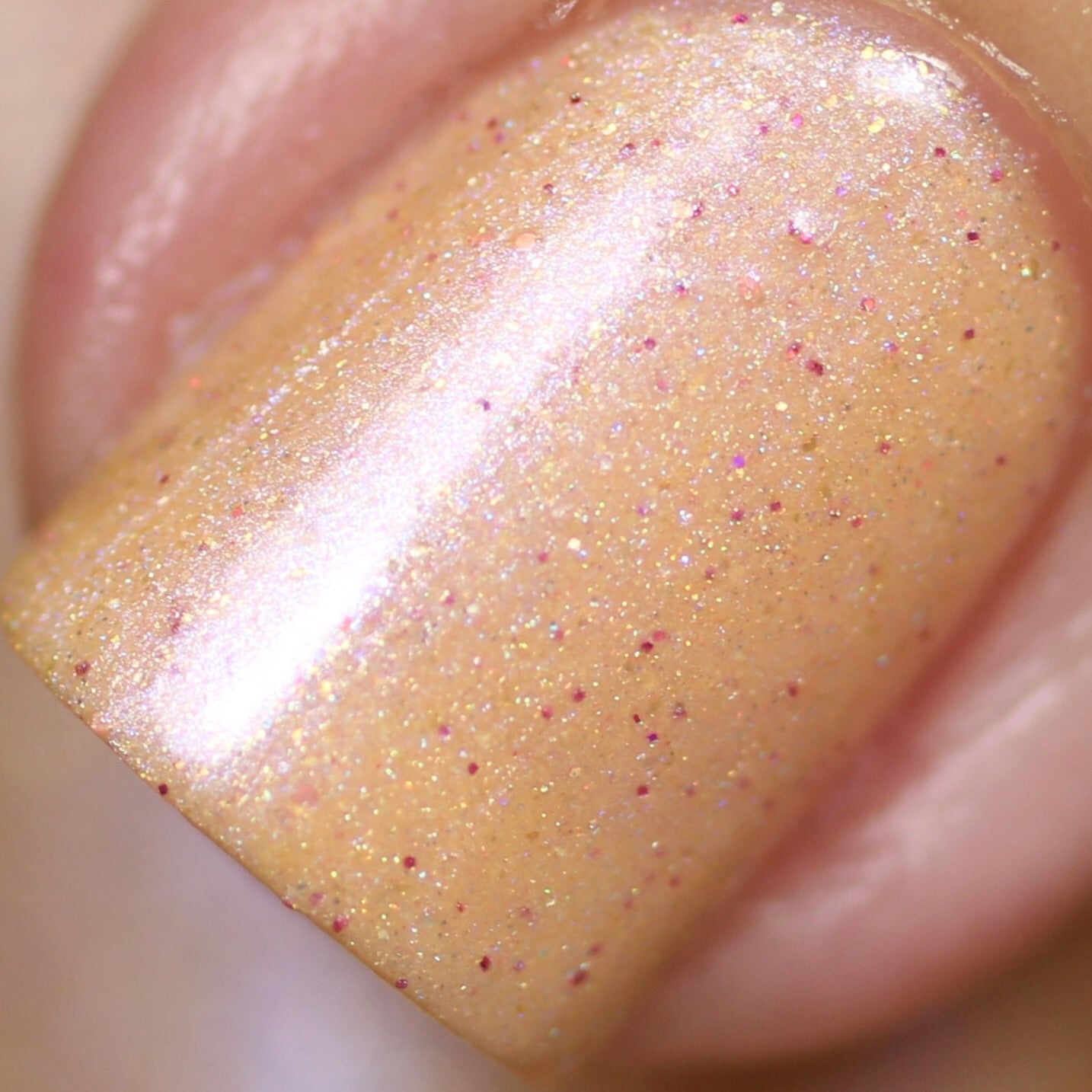 A close-up of a fingernail adorned with PI Colors' Sunrise Tellin.027 Pale Orange Nail Polish showcases the glossy finish, where tiny pink sparkles create an enchanting holographic glitter effect reminiscent of shimmery peachy-orange hues.