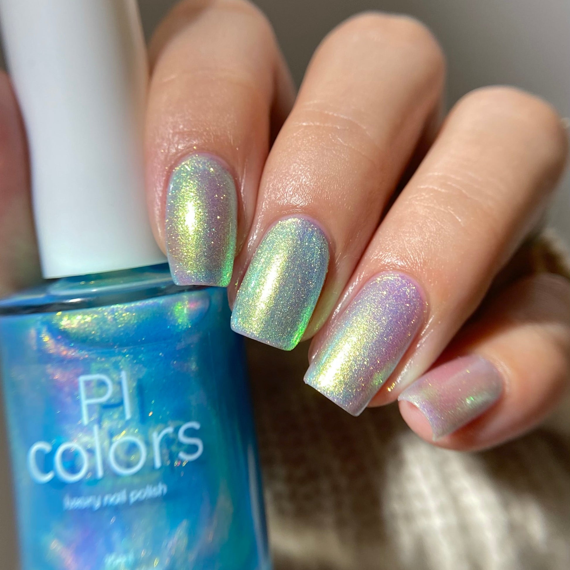 Hand with iridescent nail polish holding a bottle of PI Colors nail polish.