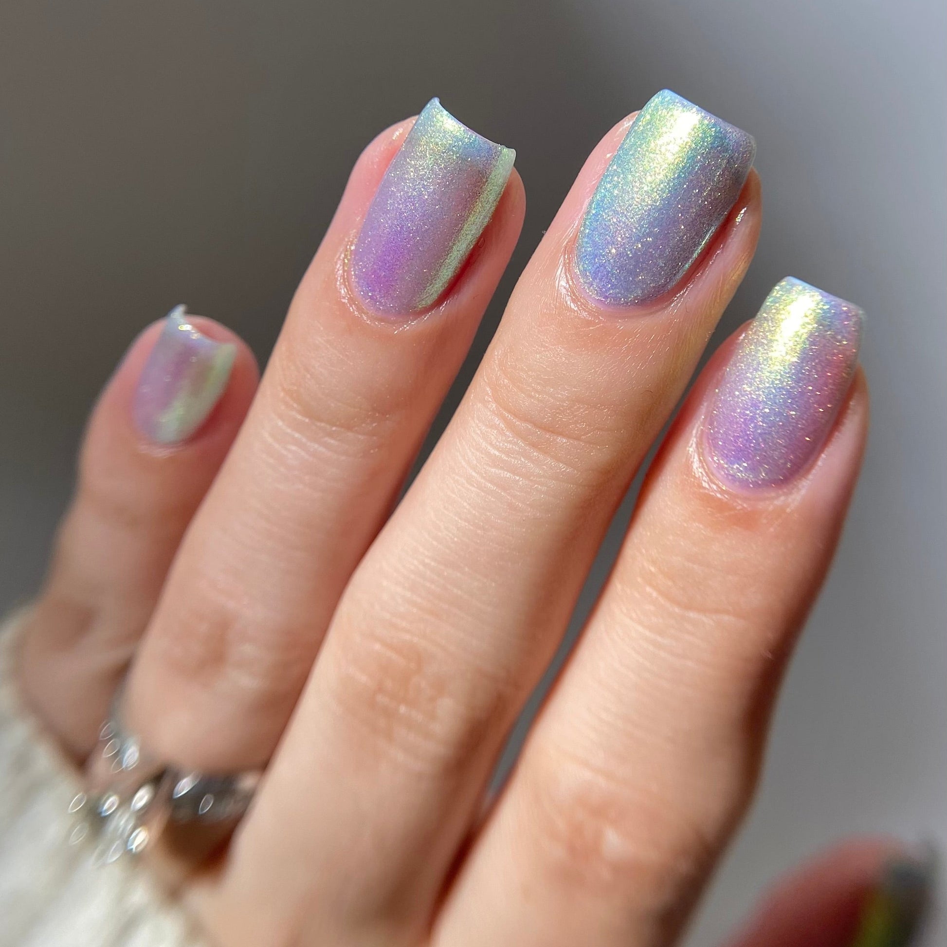 Hand with iridescent nail polish on a neutral background