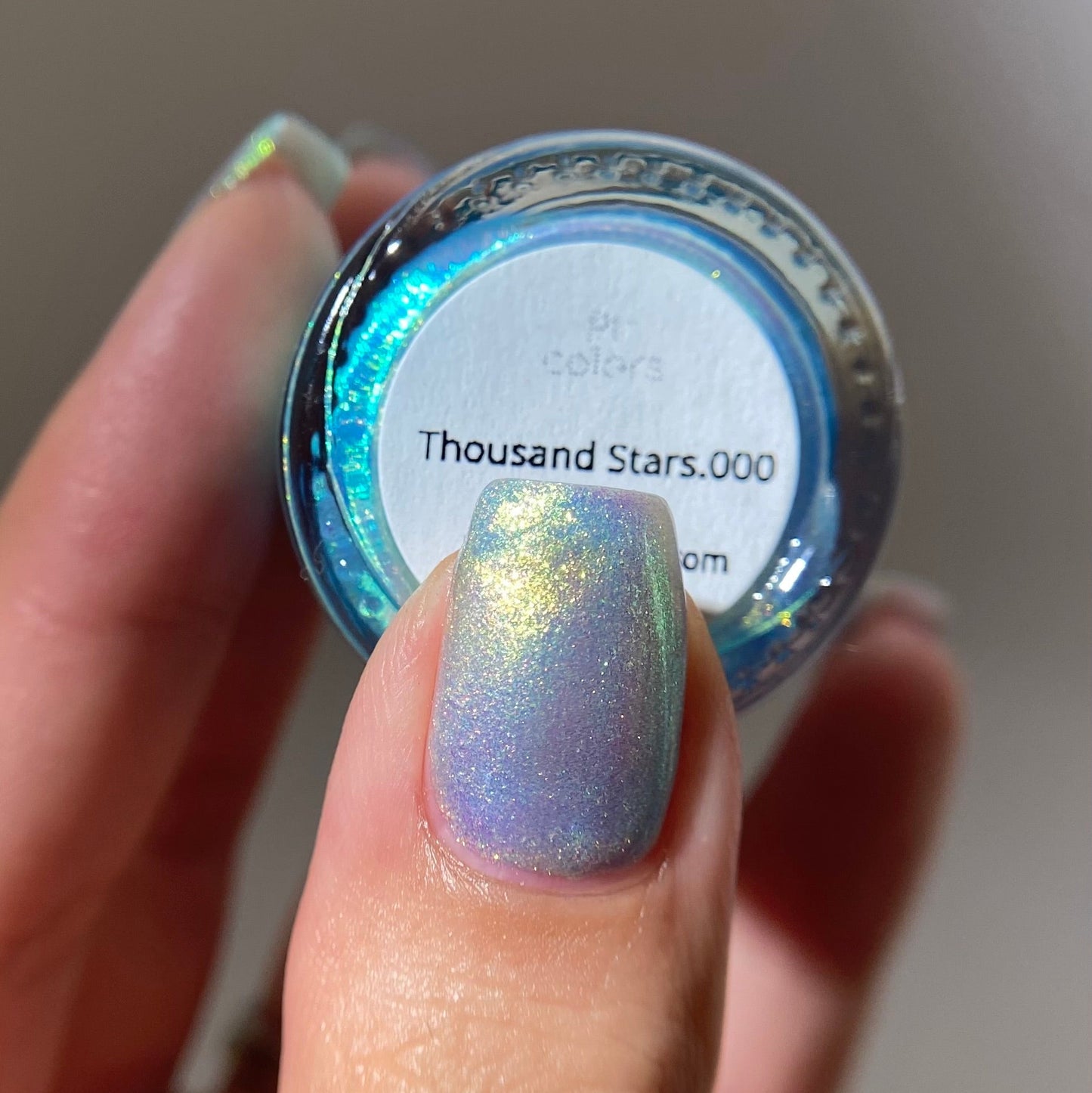 Hand holding a jar of glitter with 'Thousand Stars.000' label, showing a similar glitter on a nail.