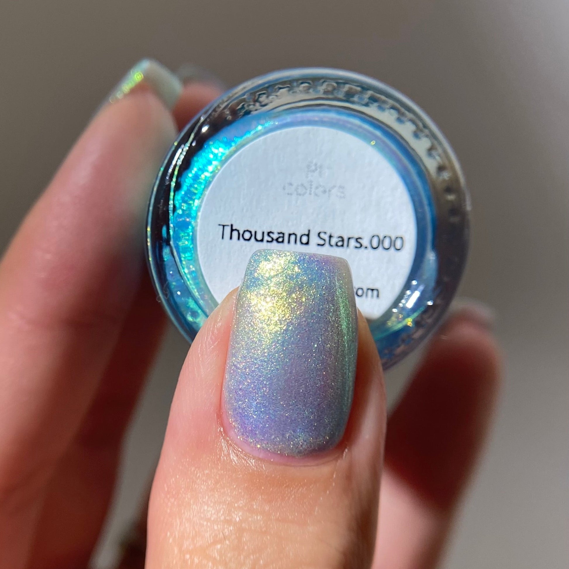 Hand holding a jar of glitter with 'Thousand Stars.000' label, showing a similar glitter on a nail.