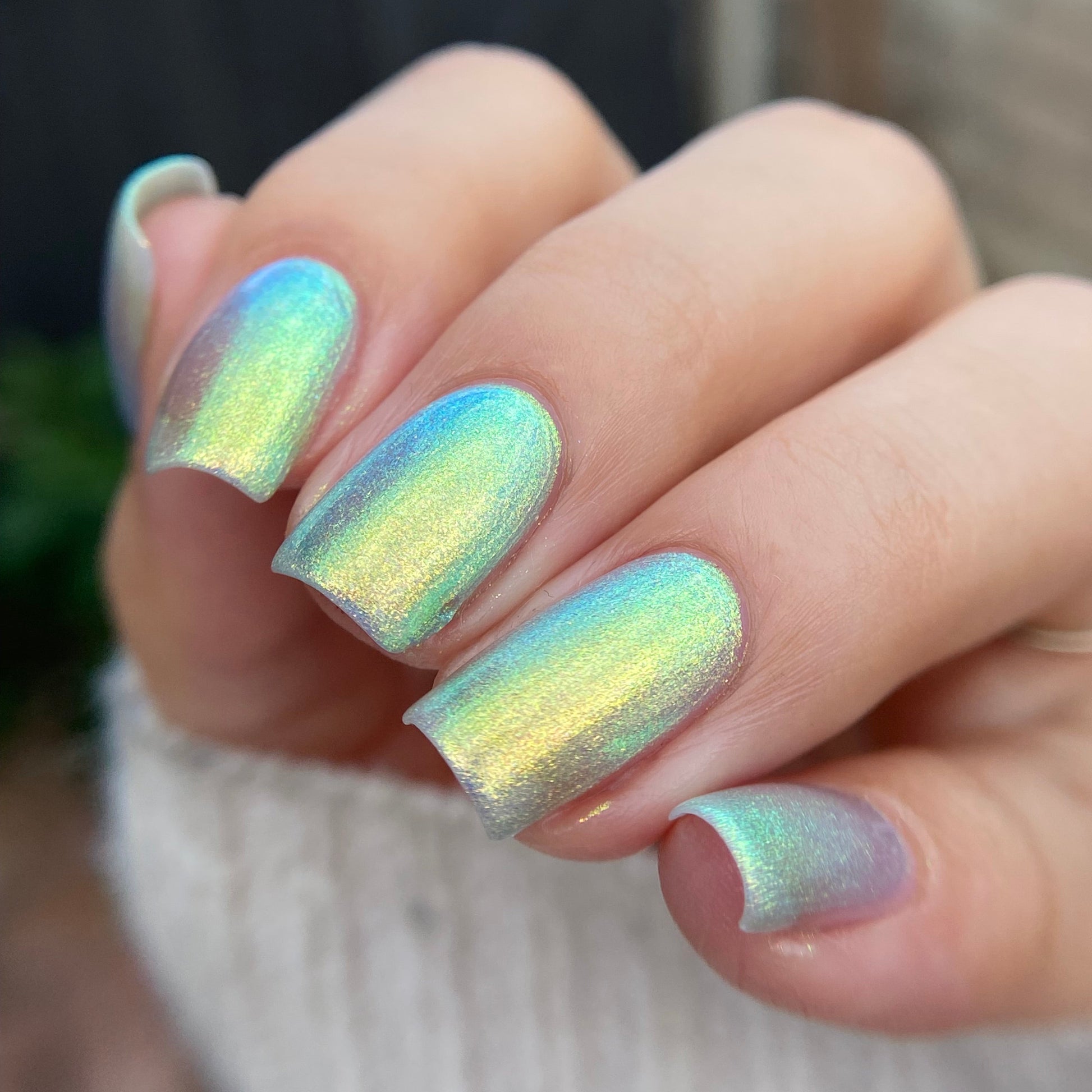 Close-up of a hand with iridescent nail polish on a blurred background