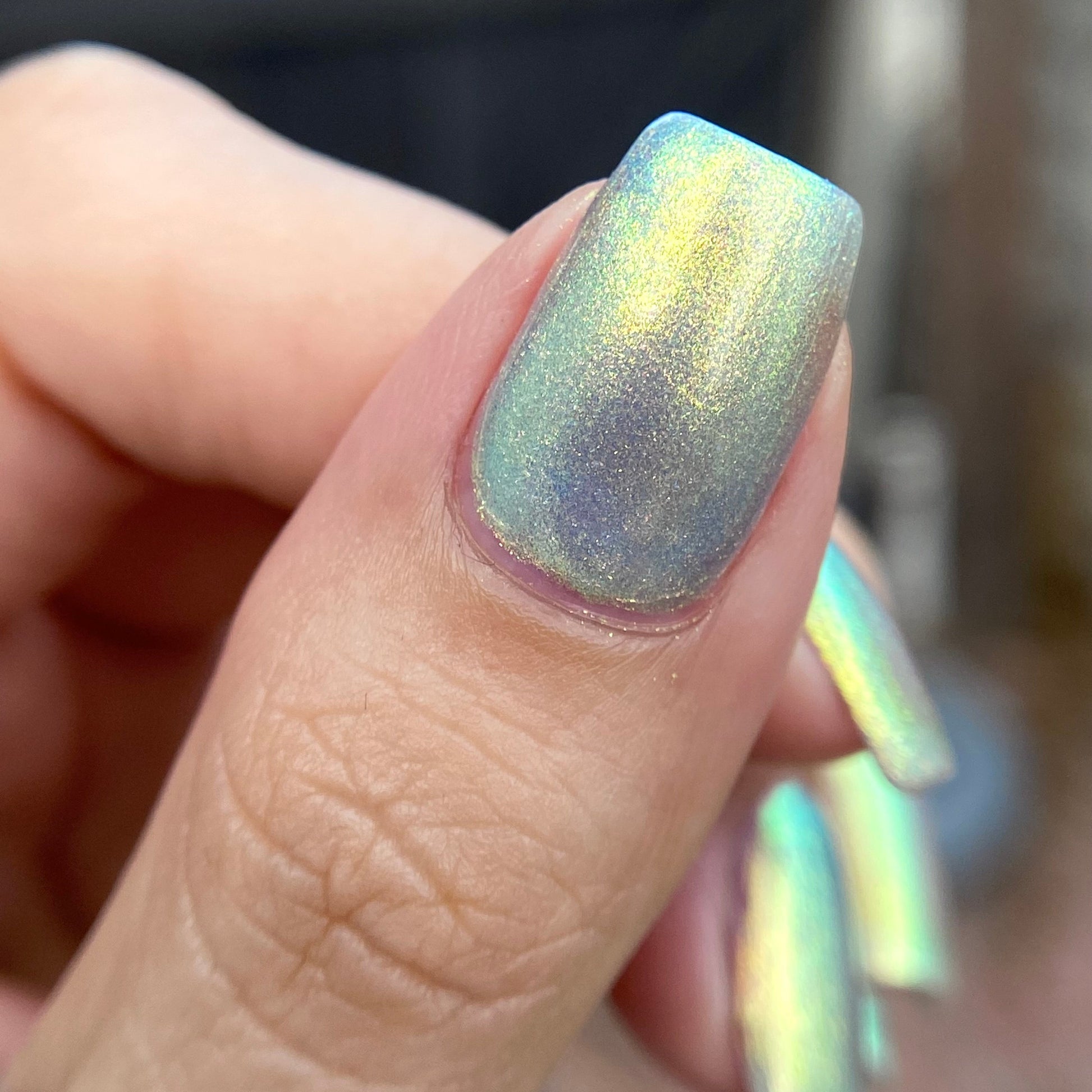 Close-up of a hand with iridescent nail polish on a blurred background