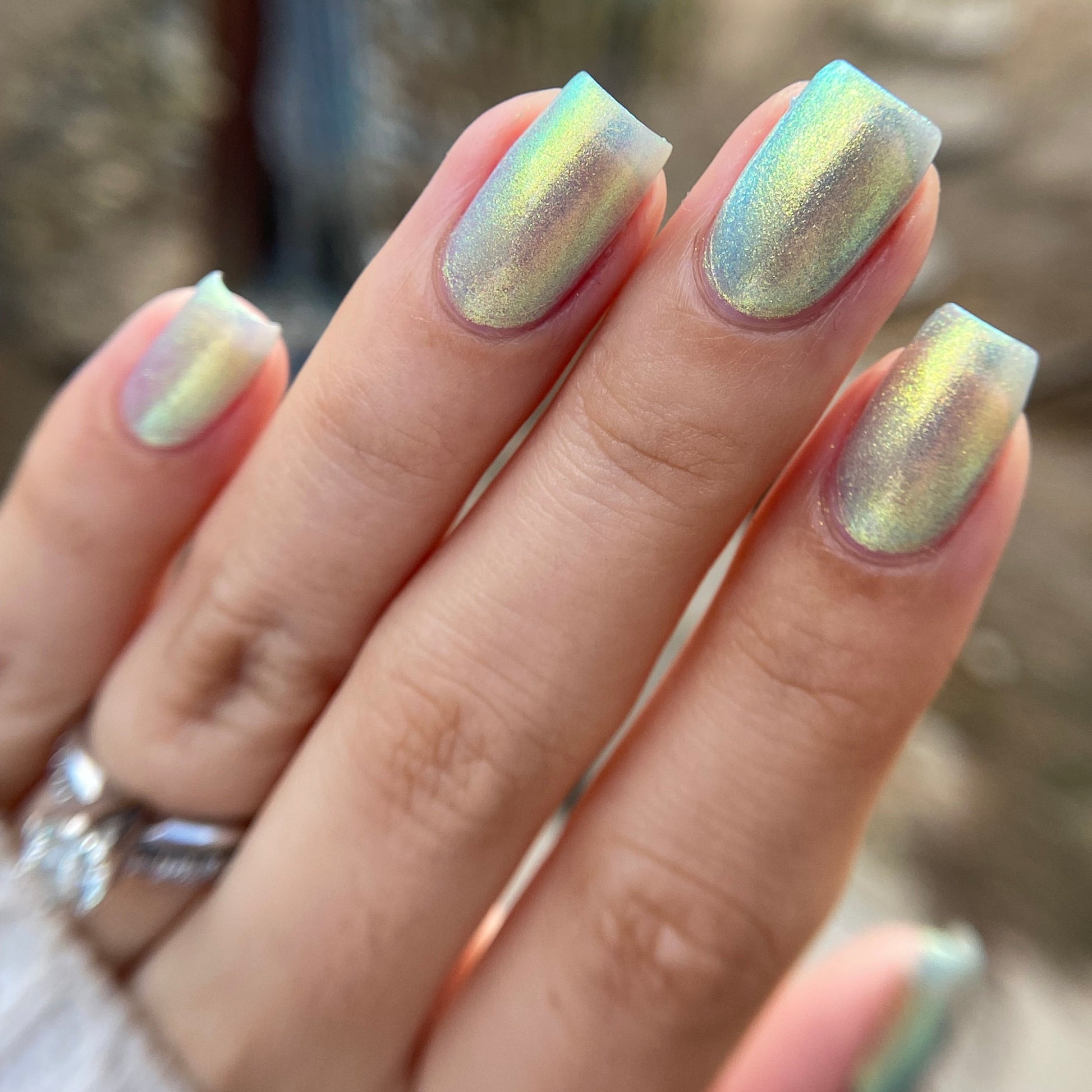 Close-up of a hand with iridescent nail polish against a blurred background