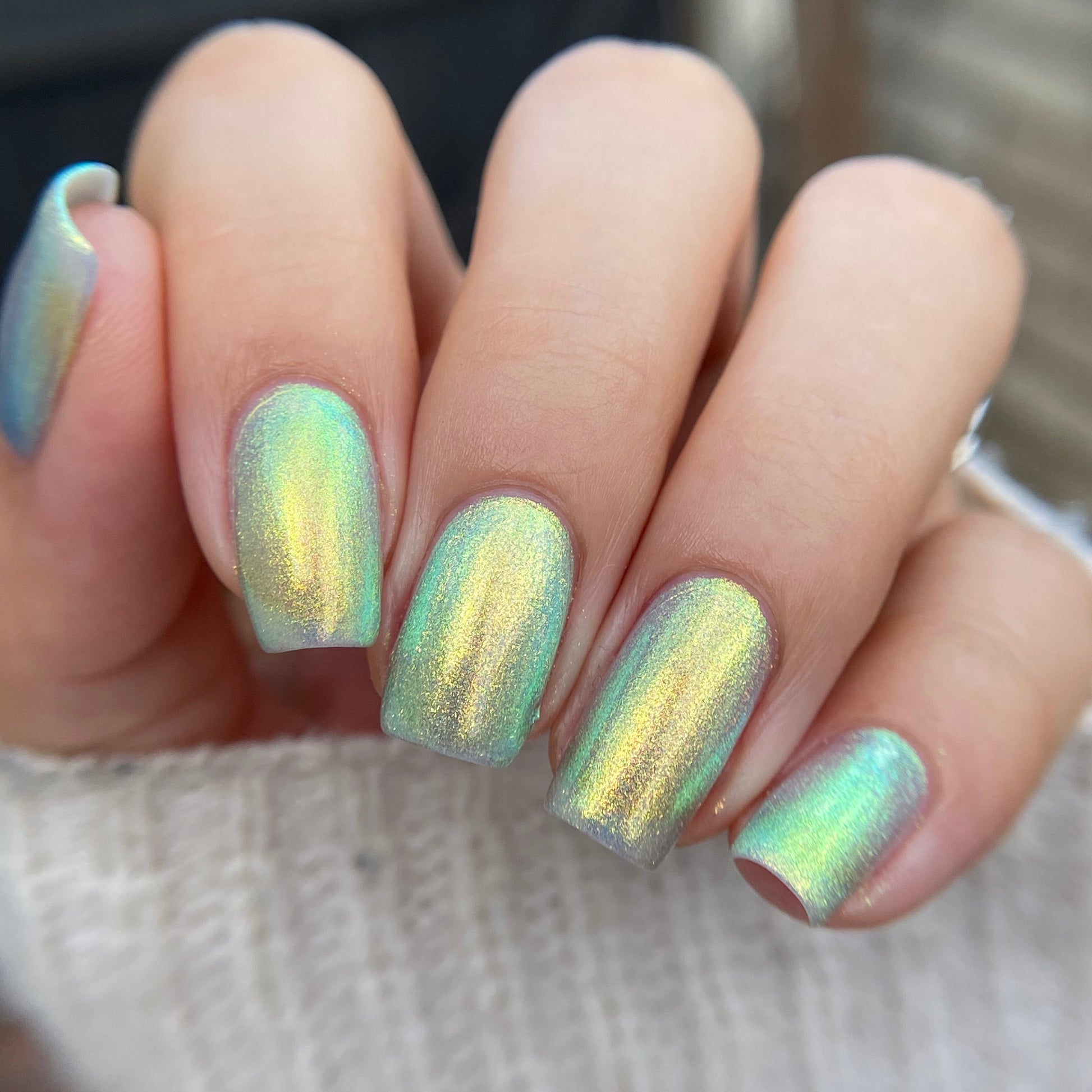 Close-up of a hand with iridescent green nail polish on a blurred background