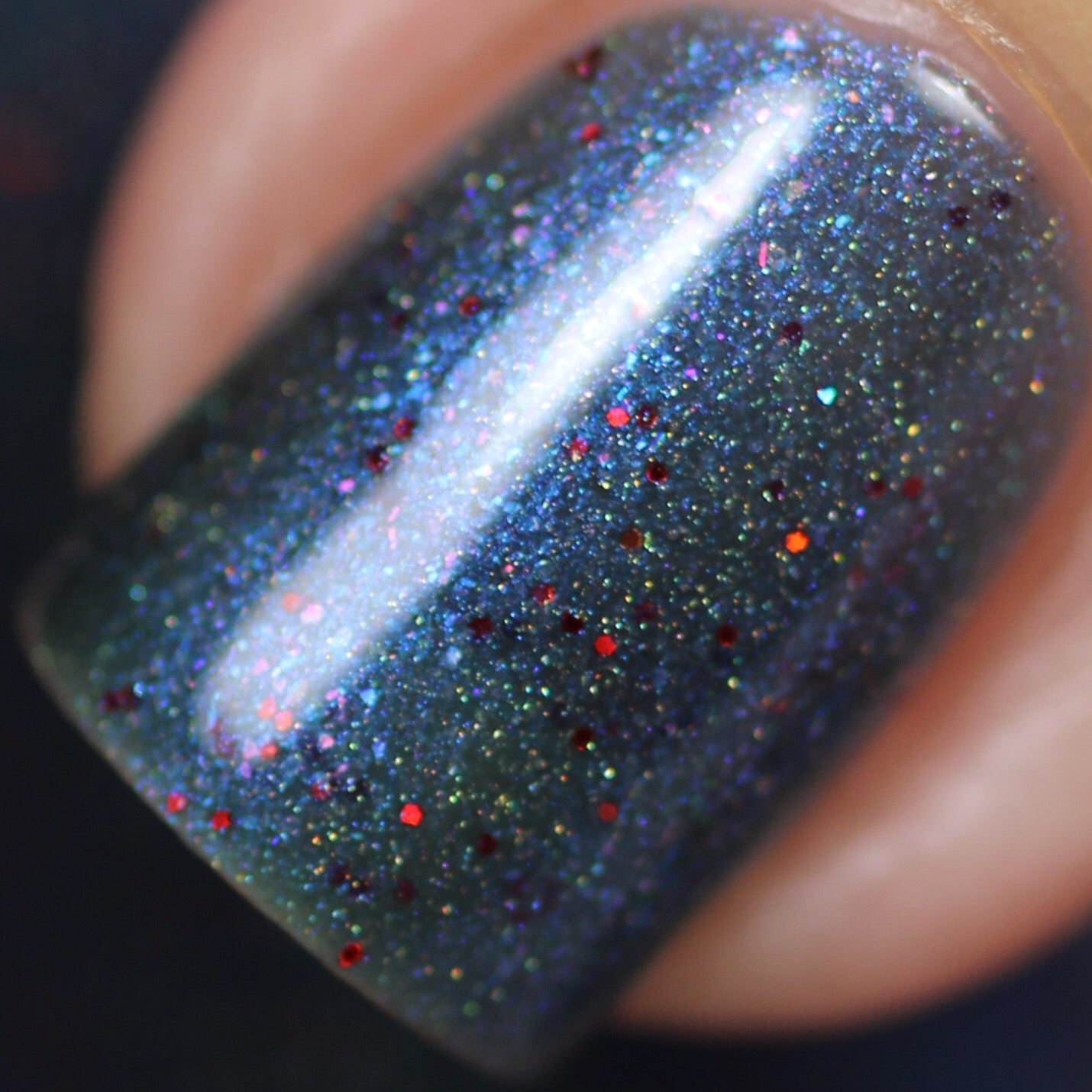 A close-up of a fingernail adorned with PI Colors' Winter Berry Blue.001 Nail Polish, featuring a shimmering dark gray base infused with vibrant blue, red, and silver glitter along with holographic powder for a sparkling and textured look.