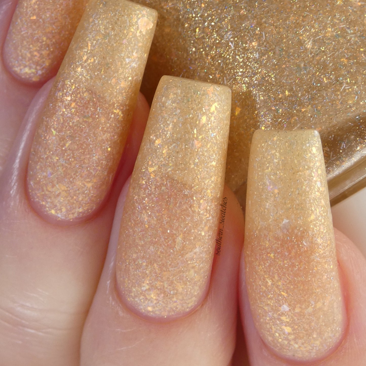 Close-up of fingernails painted with the Honey Bee.060 Gold Nail Polish Topper by PI Colors, enriched with color-shifting flakes. The reflective, glittery texture enhances the look of the neatly manicured nails, giving them a dynamic and multidimensional finish.
