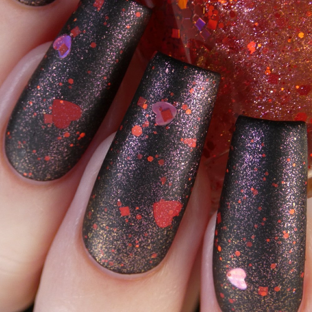 Close-up of nails adorned with PI Colors' Strawberry Heart.208 Red Nail Polish Topper, featuring matte black as the base. The red glitter and holographic heart-shaped flakes offer a sparkling contrast, resulting in a striking and festive appearance, all while being 10-free.