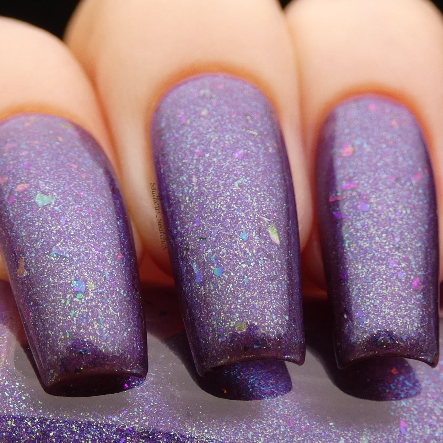 Close-up of fingers with long nails painted in PI Colors' Arsu.111 Deep Purple Nail Polish, showcasing color-changing effects. The vibrant finish is enhanced with colorful shimmer and small iridescent flakies, creating a glossy and sparkling texture.