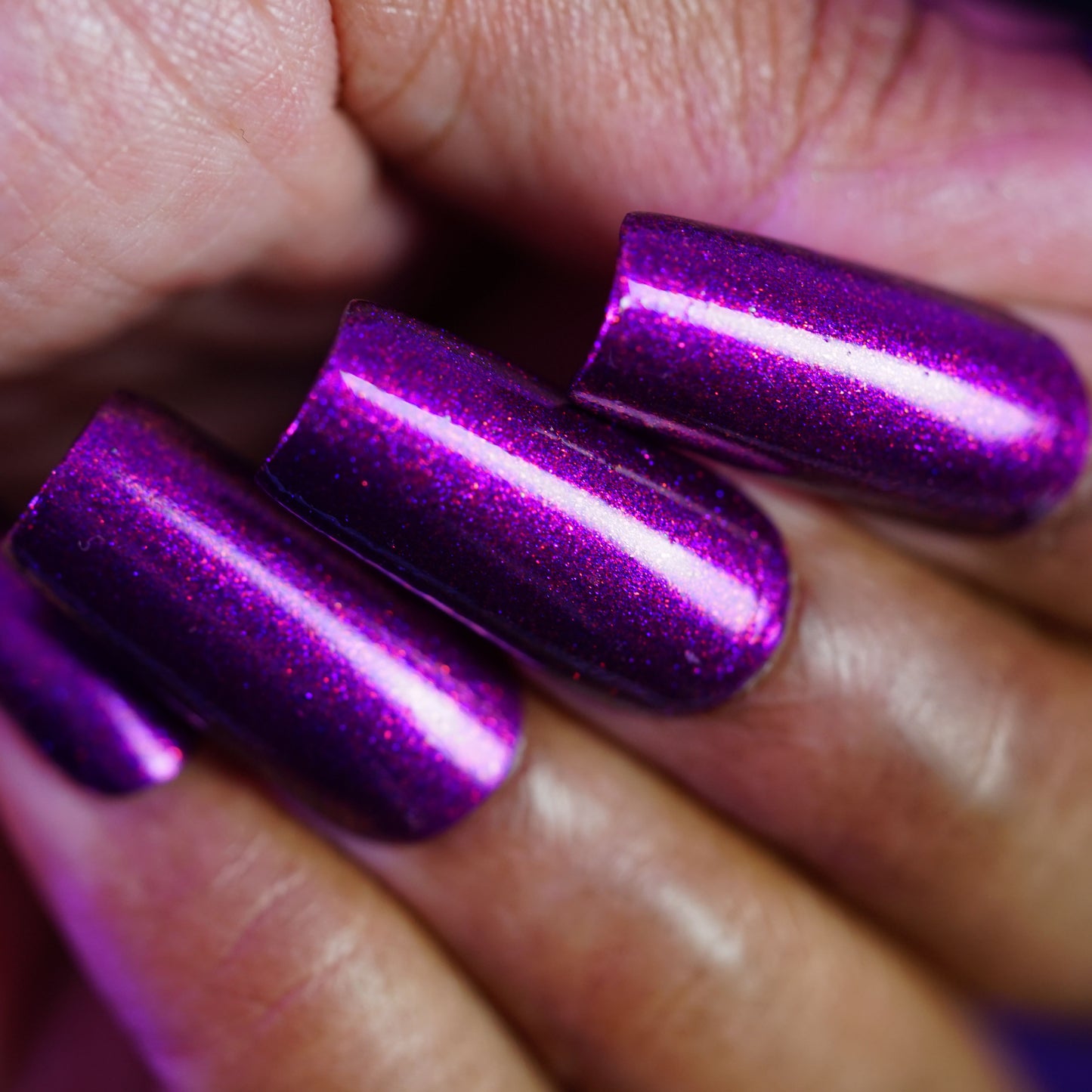 Fingers with long, glossy nails painted in PI Colors’ Aubergine.100, a deep purple lacquer with glitter shimmer, create a smooth, shiny finish that flatters medium brown skin.