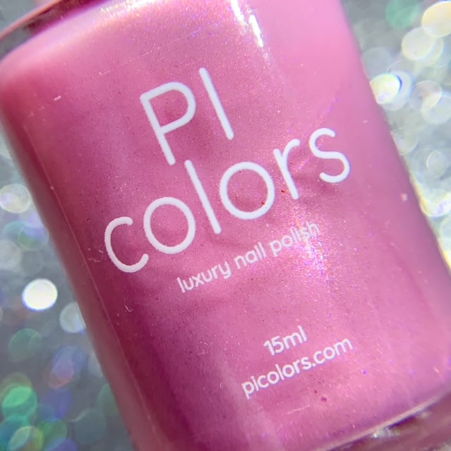 Close-up of a handmade electric pink nail polish bottle labeled "Water Lily.317 by PI Colors, luxury nail polish 15ml, picolors.com" against a sparkling, blurred silver background.