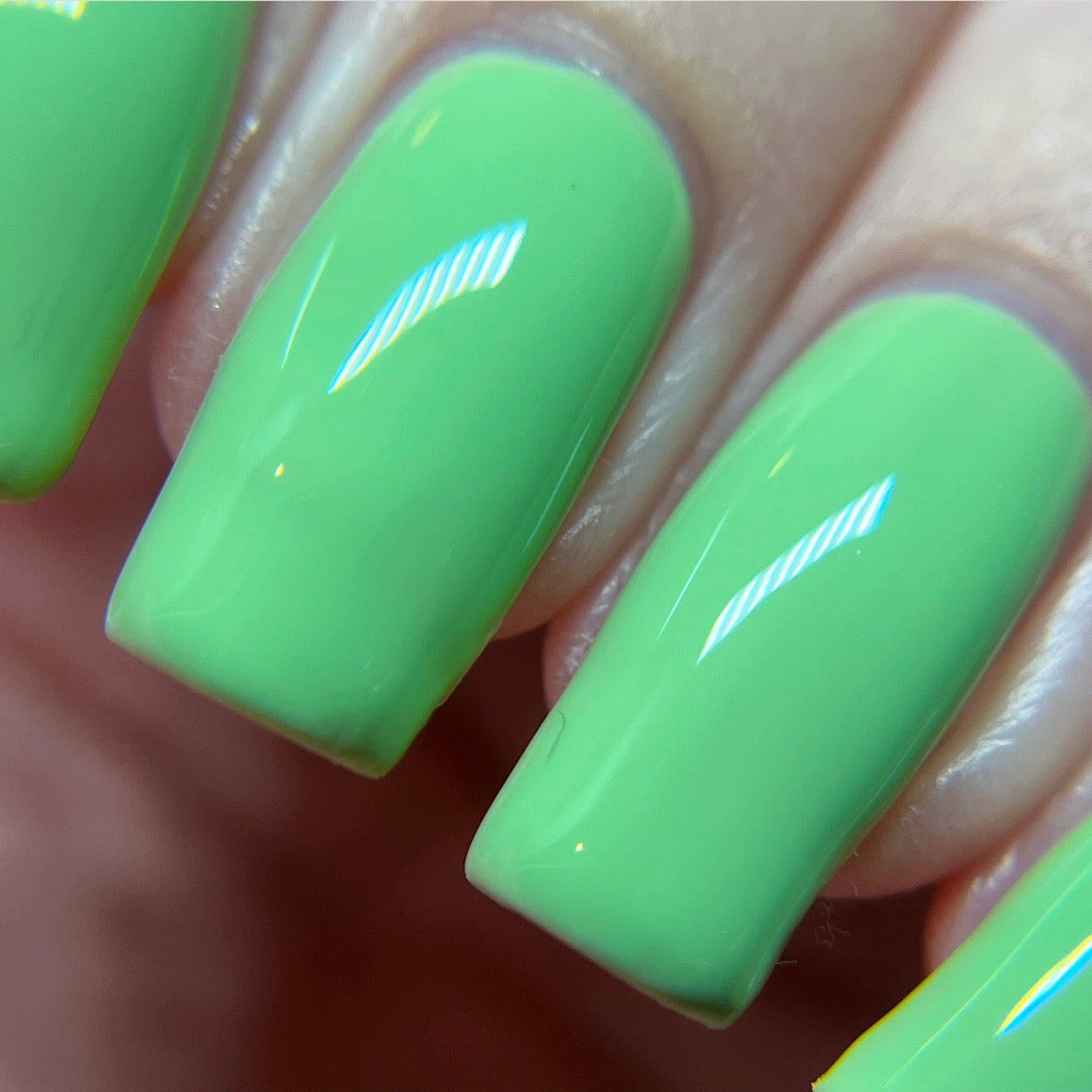 Close-up of four fingernails adorned with PI Colors Pistachio.400 Green Nail Polish, exhibiting a shiny, bright pistachio shade. The crème finish catches the light and emphasizes their smooth texture.