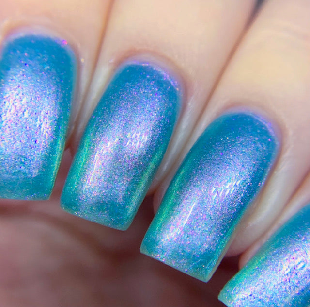 A close-up of fingers adorned with PI Colors' Ocean Whitecap.309 Blue Nail Polish, featuring handmade, holographic iridescent shades of blue, purple, and green. The shiny metallic finish beautifully reflects light, showcasing color-changing effects that create a stunning gradient across the nails.