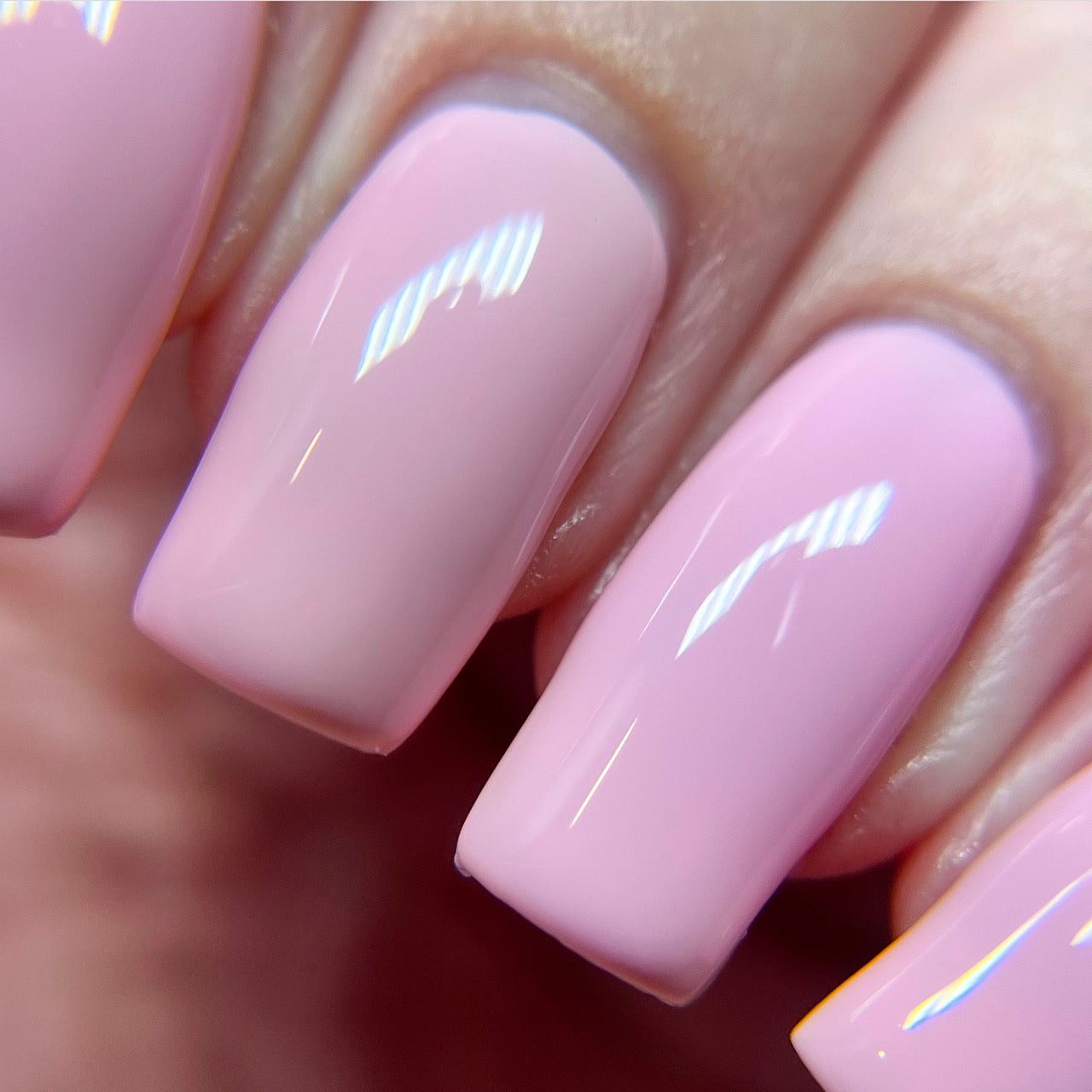 A close-up of impeccably manicured nails adorned with the glossy pastel pink hue of Cupcake.400 Pink Nail Polish by PI Colors. The smooth creme finish brilliantly reflects light, accentuating the clean edges and uniformity of this luxury nail lacquer application.