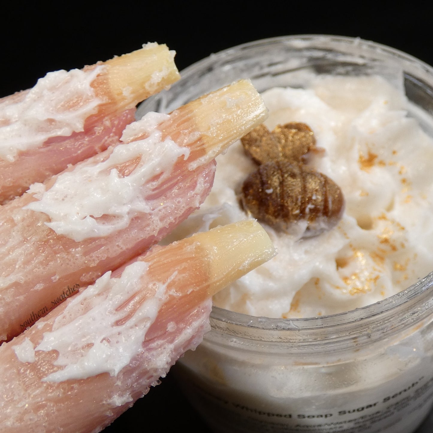 A close-up reveals fingers with long nails immersed in the Honey Scented Whipped Soap Sugar Scrub by PI Colors, a creamy white blend reminiscent of whipped soap. Nearby is a jar filled with this fragrant concoction, adorned with a small gold-colored decorative piece on top.
