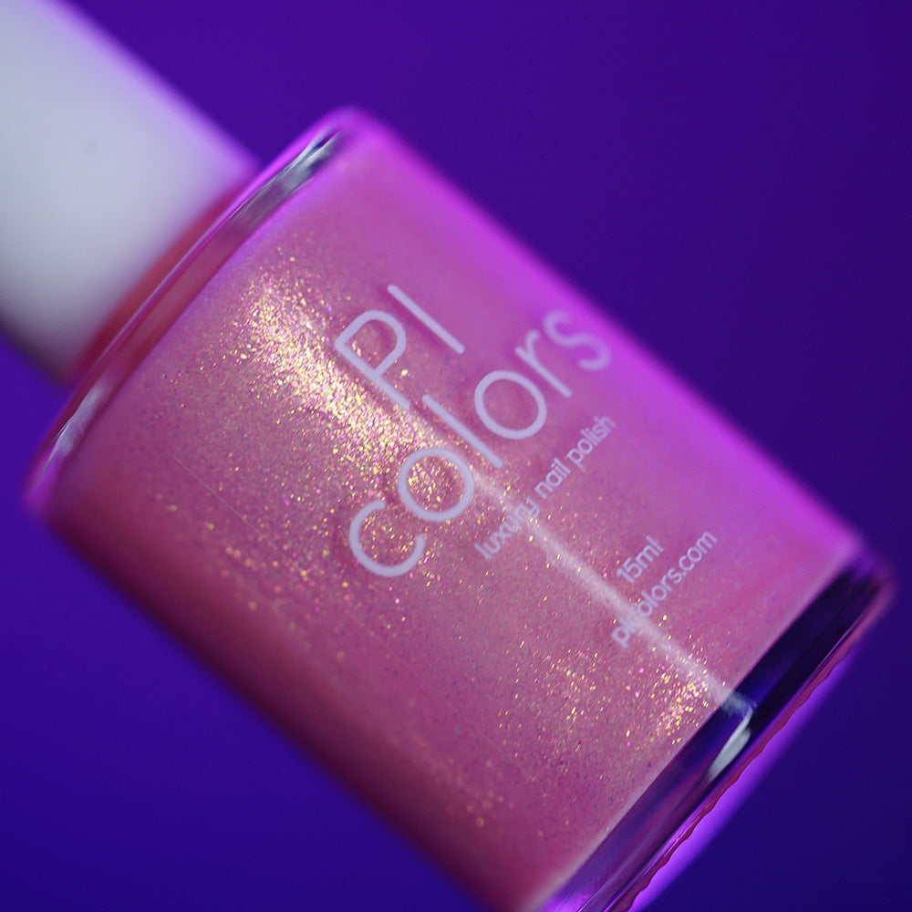 A close-up of a tilted bottle of PI Colors Lemon Pink Sugar Cookie.422 handmade nail polish in a shimmery pink shade, set against a vibrant purple background.